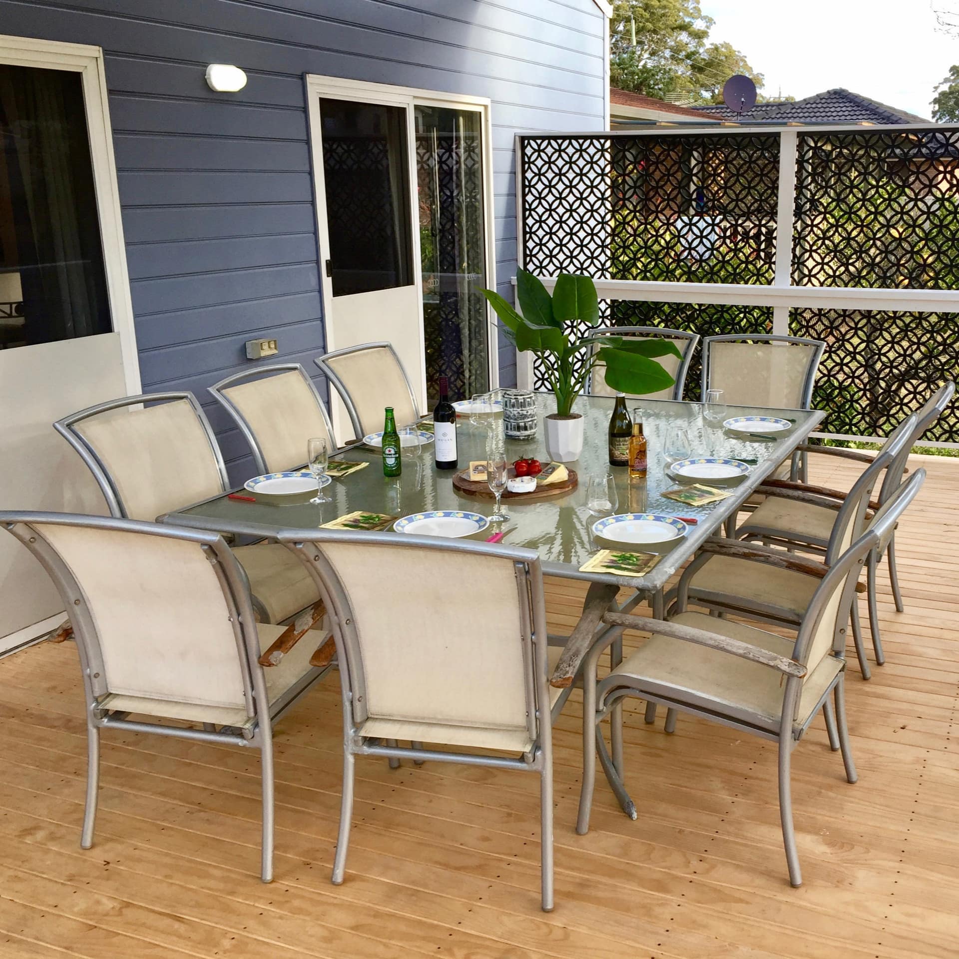 A wooden deck of a blue cottage with a glass dining table set with plates.