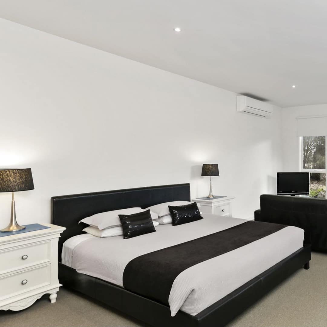 Spacious bedroom with black-and-white decor, beige carpet, king-size bed, sitting area with flat-screen TV and tall windows.