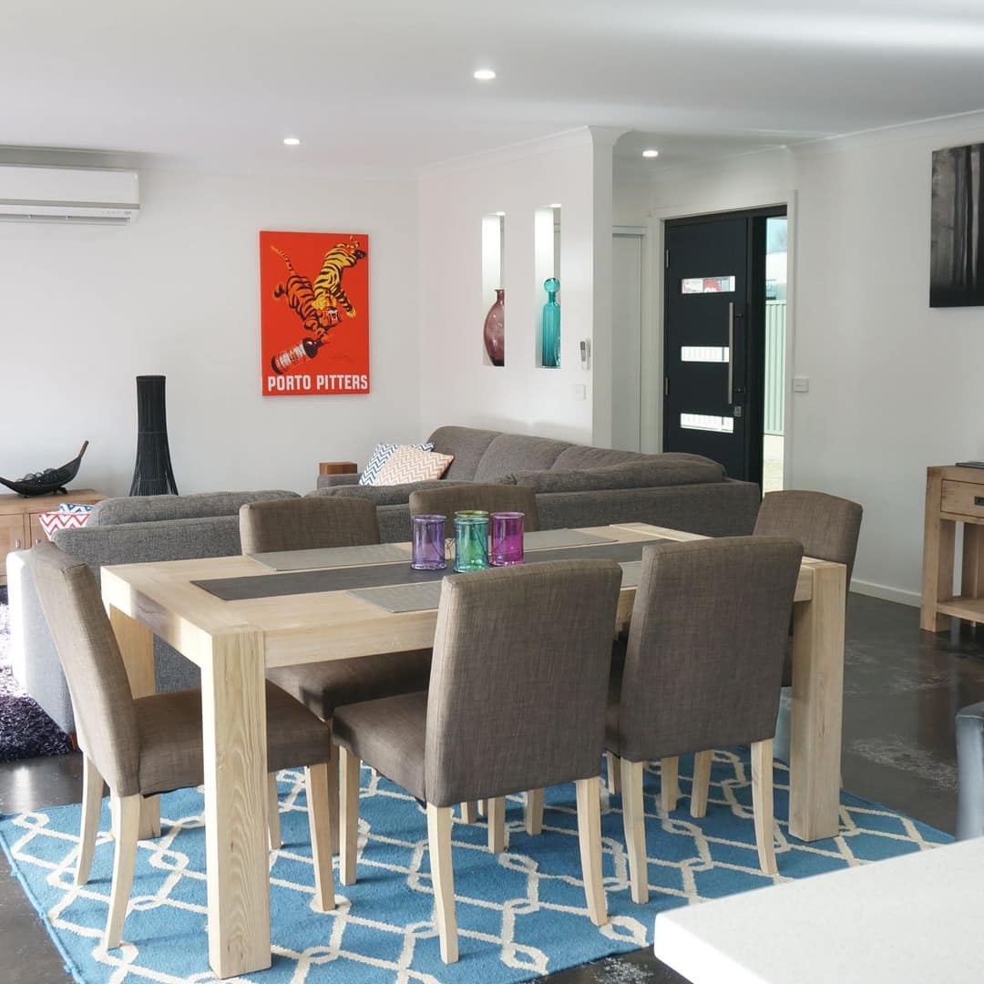 Open dining and living room, grey stone floor, wood dining set, grey canvas L-shaped sectional, and shag rug.