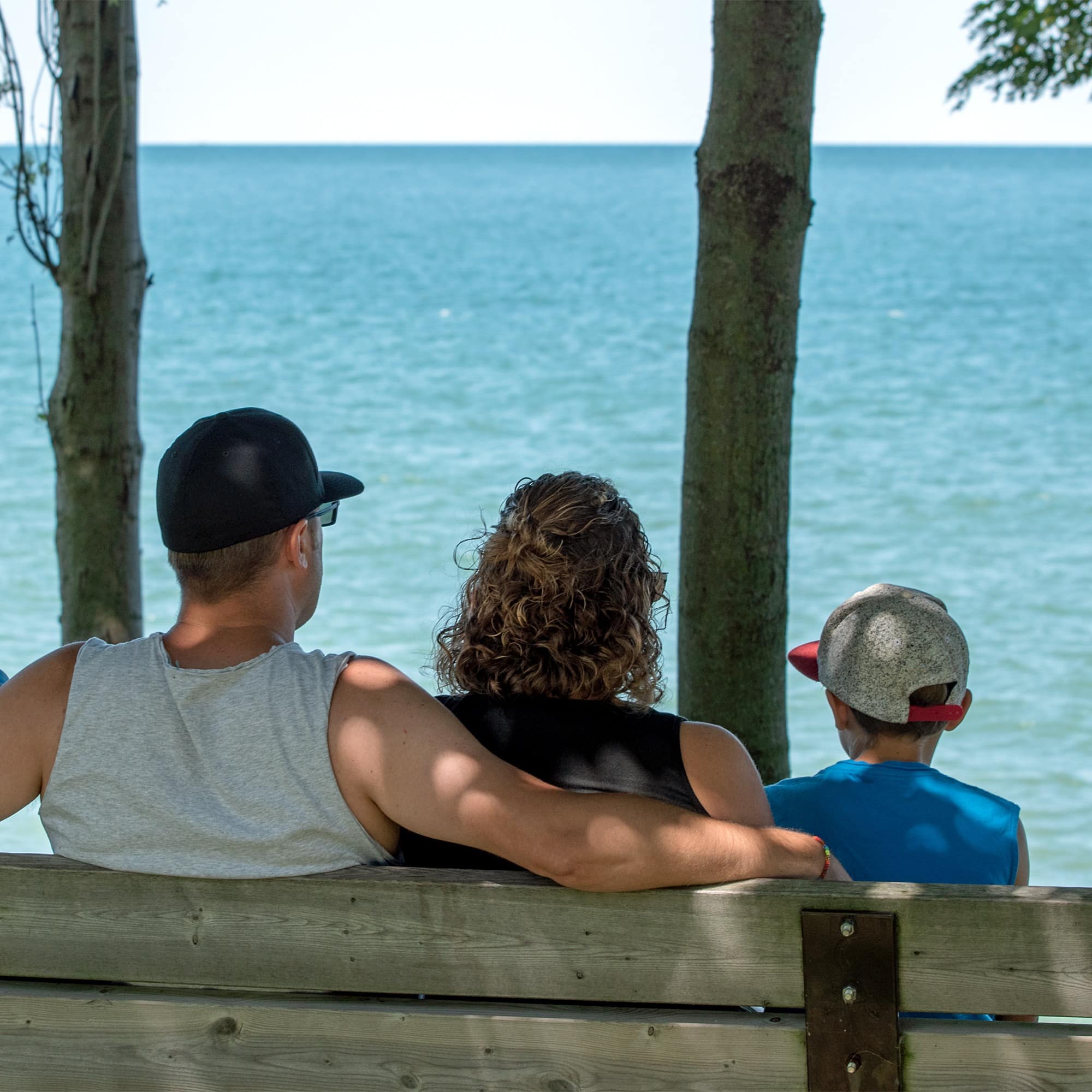 Family of four sitting on park bench looking out at water under shade tree
