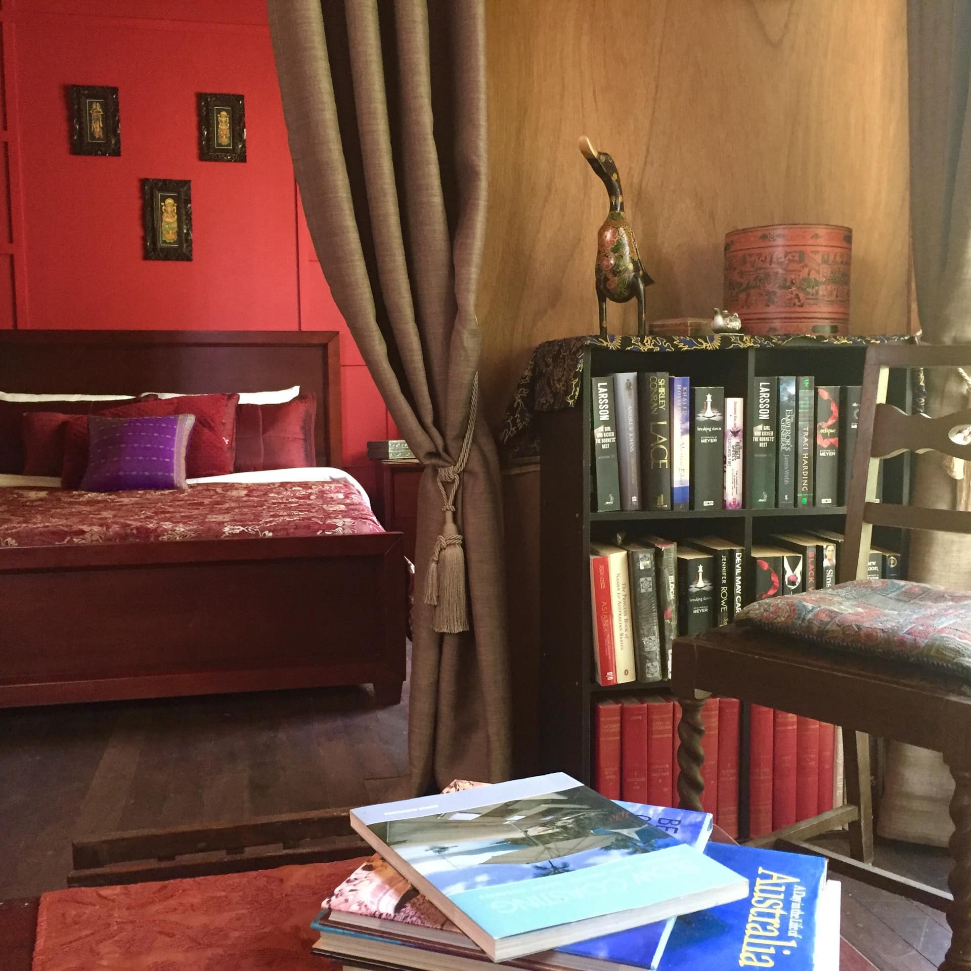 Luxurious king-sized bed with burgundy linens in 1-bedroom cabin with red walls, small library with chair and hardwood floors