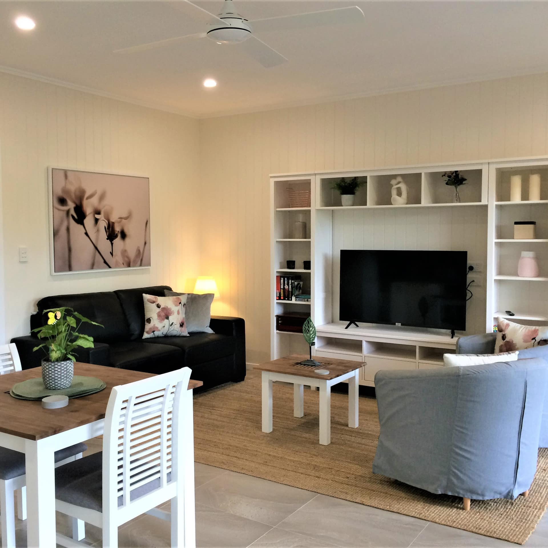Open dining and living room with grey tile floors, black sofa, round blue chairs, and flatscreen TV framed by bookshelves.