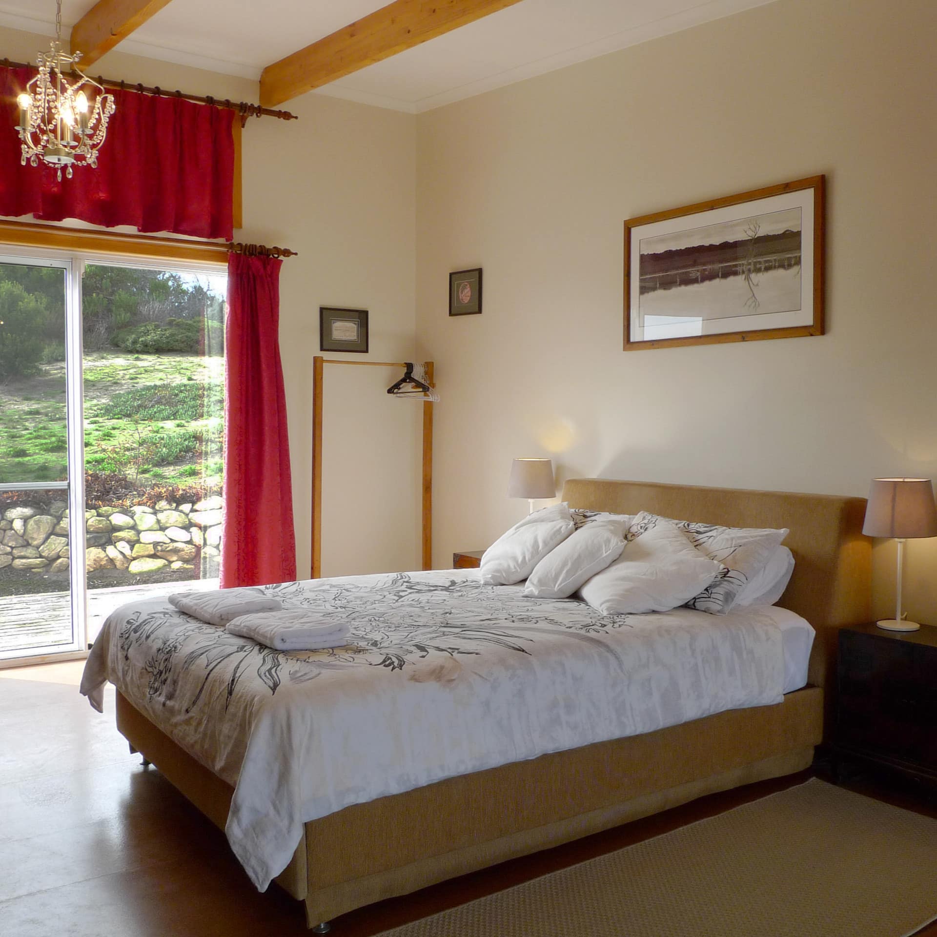 Spacious bedroom with a king size bed, white floral bedding, and sliding glass doors to a patio space with red curtains.
