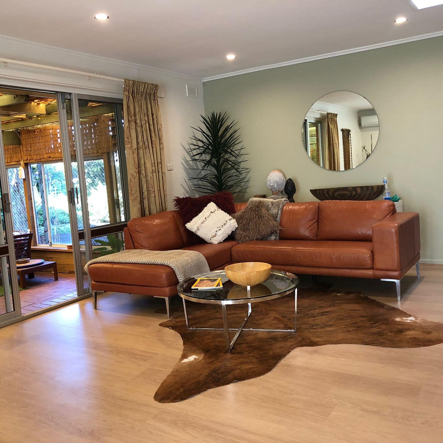 Open living room with hardwood floors, light green walls, a brown leather sectional, cowhide rug, and glass doors to patio.