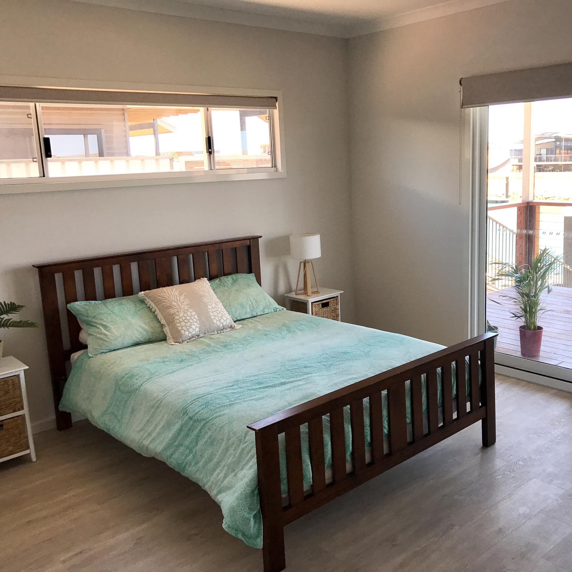 Bedroom with hardwood floors, a wood-framed king size bed, teal bedding, glass sliding doors to a balcony with canal views.