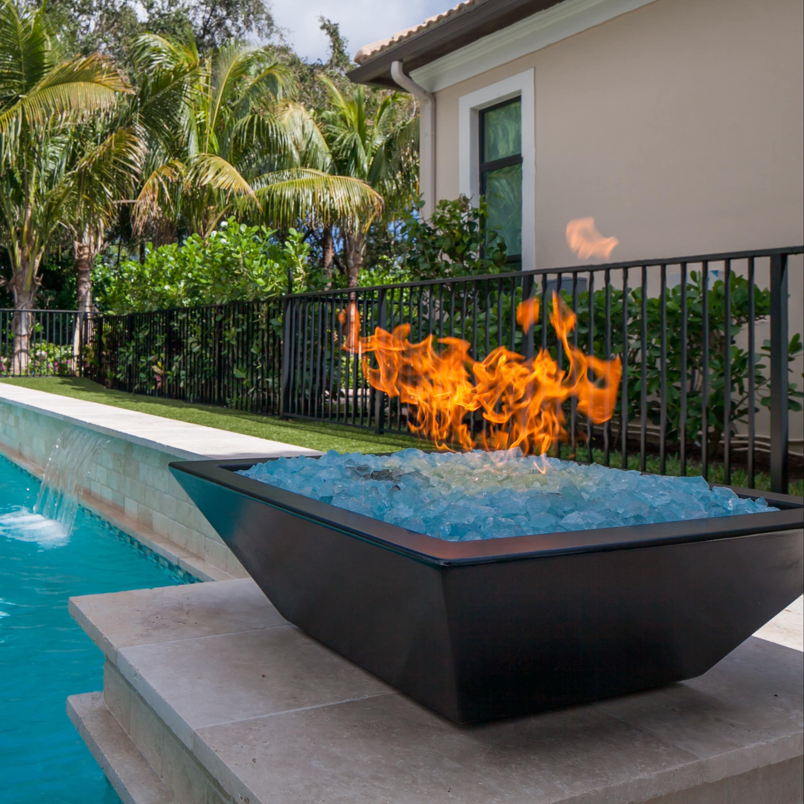 Gas fire pit next to a pool with waterfall in backyard
