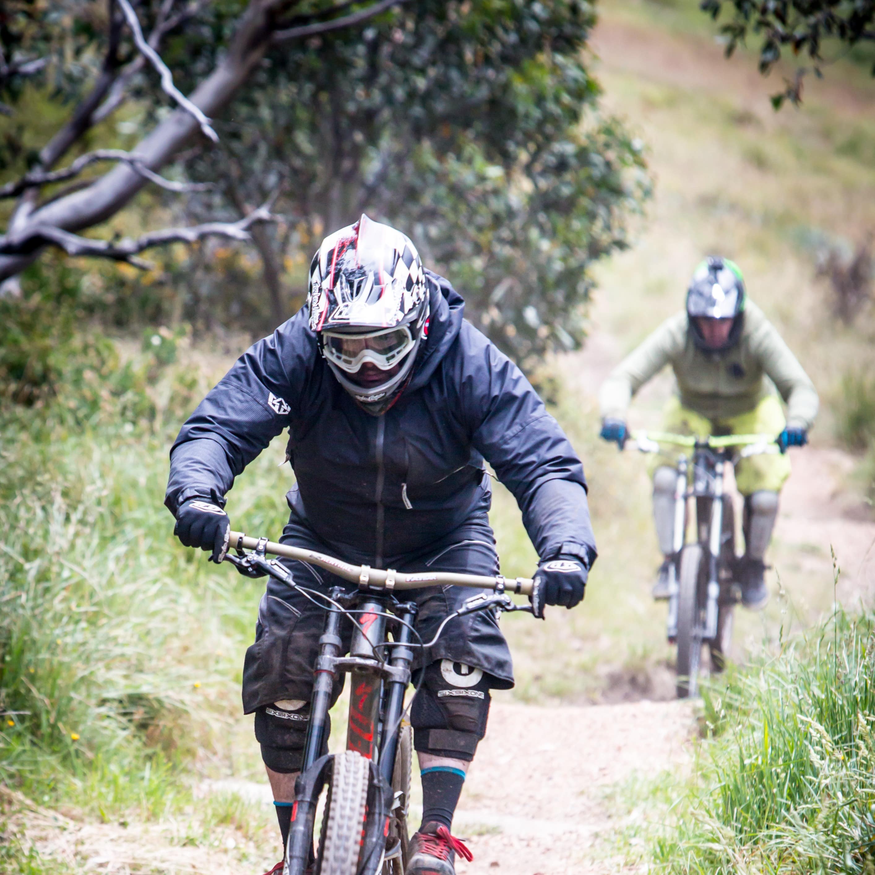 Two mountain bike riders coming down bumpy trail in Australia with brush and trees on the side