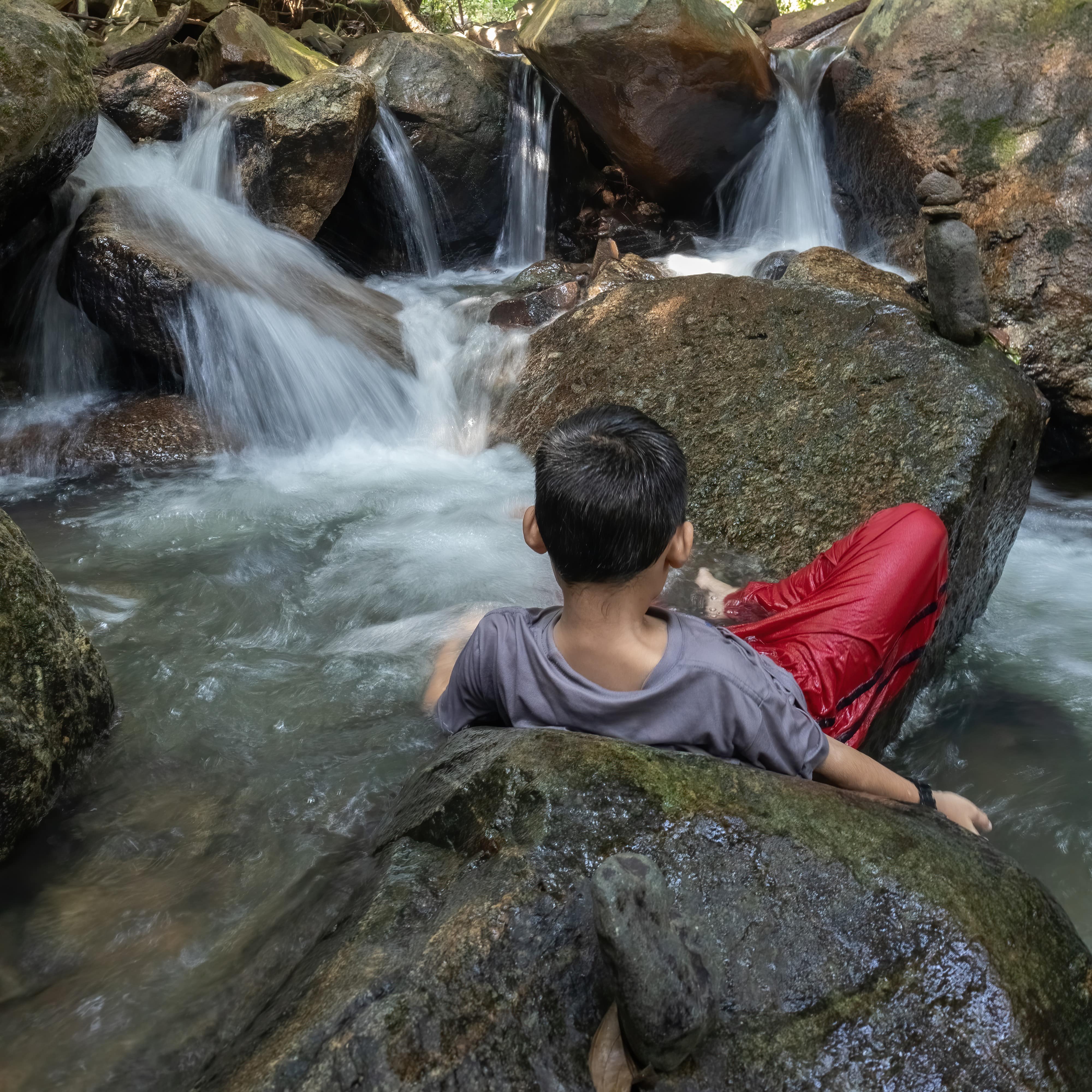Young boy sitting on rocks in the stream in the jungle