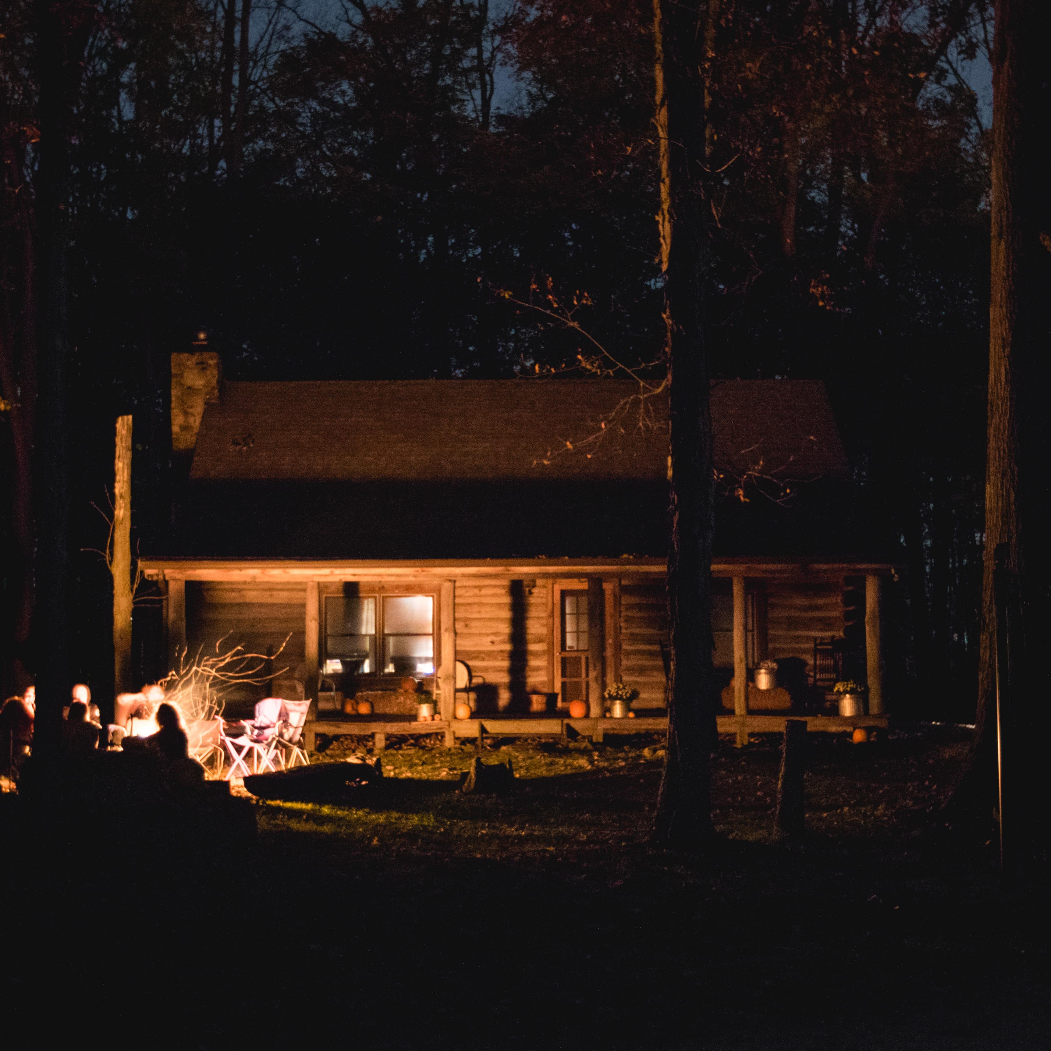 Travellers enjoying a campfire in the front yard of a log cabin surrounded by trees