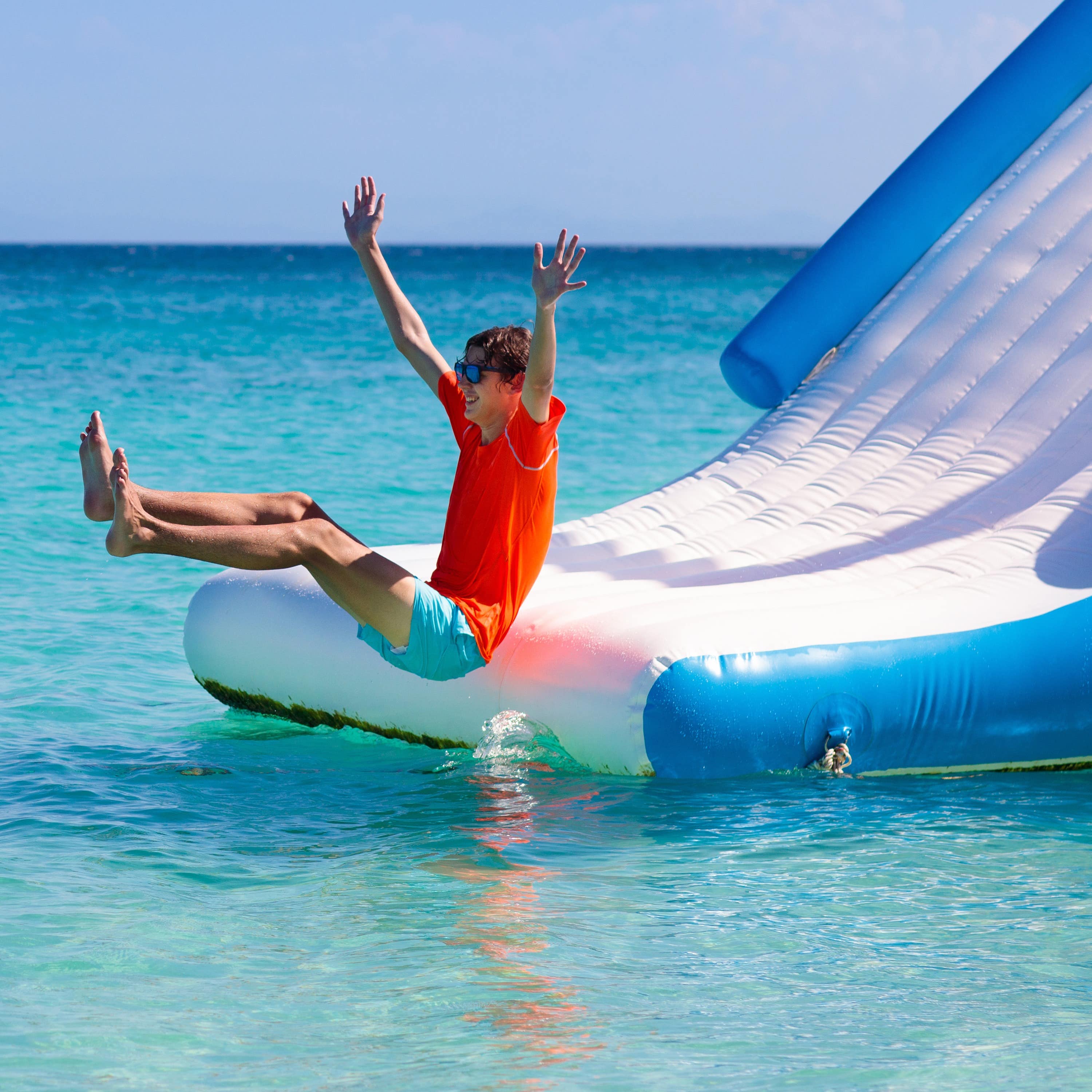 Young teen with sunglasses on sliding down water trampoline into ocean