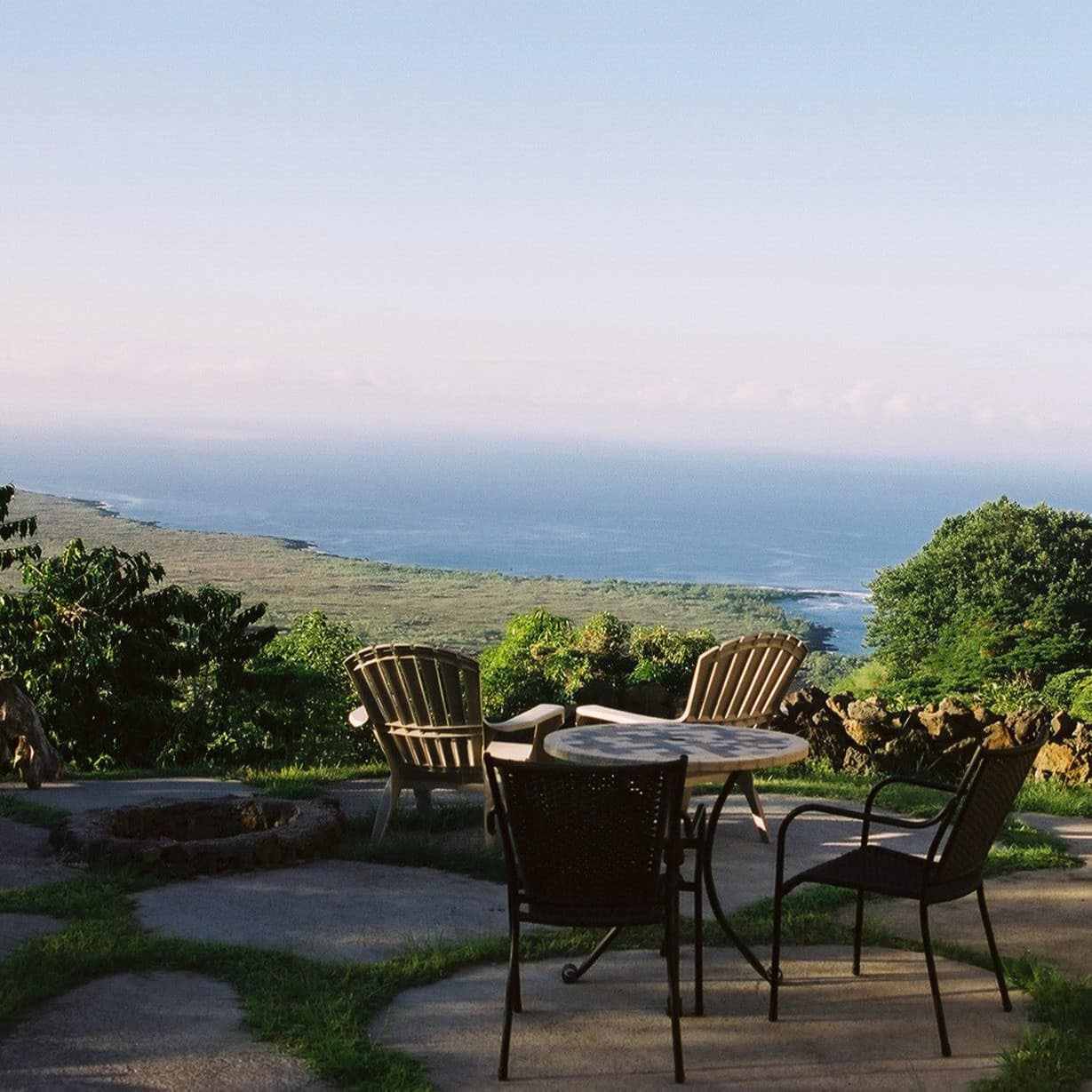 A stone patio space with lounge chairs and a bistro dining set overlooking a panoramic view of the ocean.