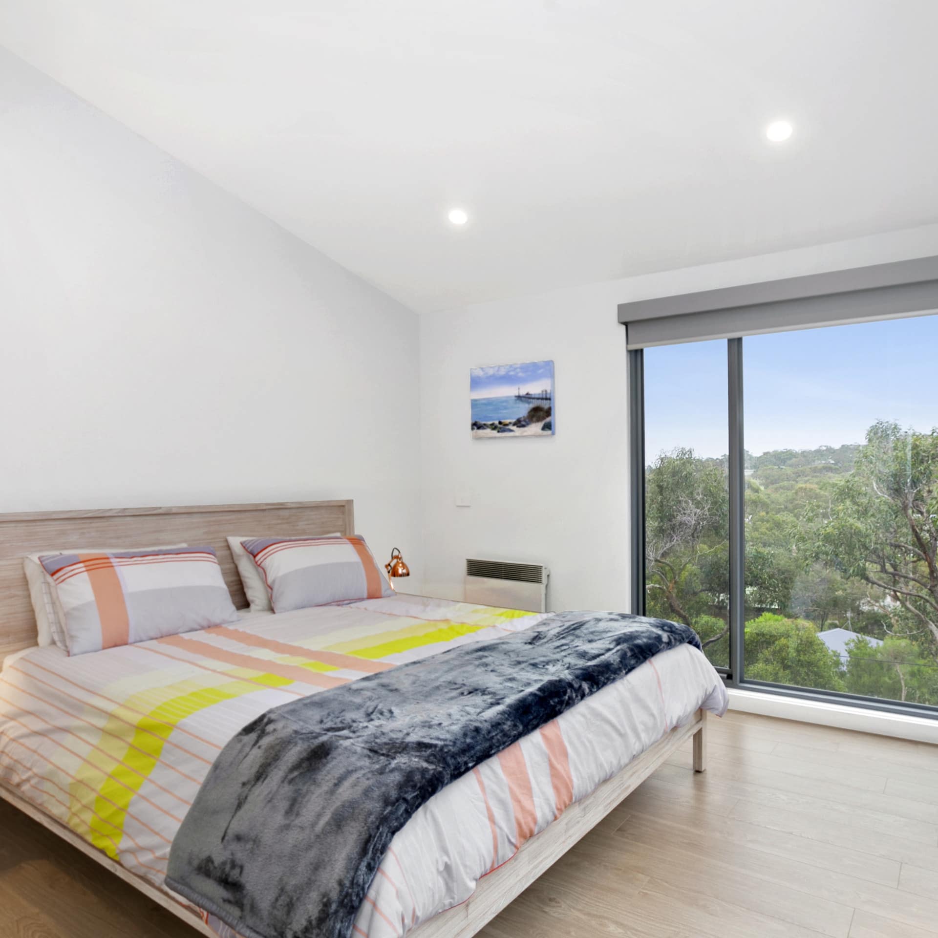 Spacious bedroom with a wood-framed king size bed, orange and yellow bedding, tall windows with bush views.