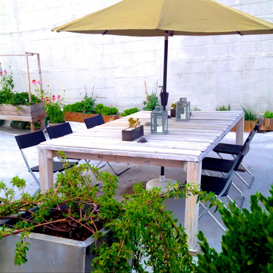 Bright patio space with a wooden dining set, yellow umbrella and lush plant beds.