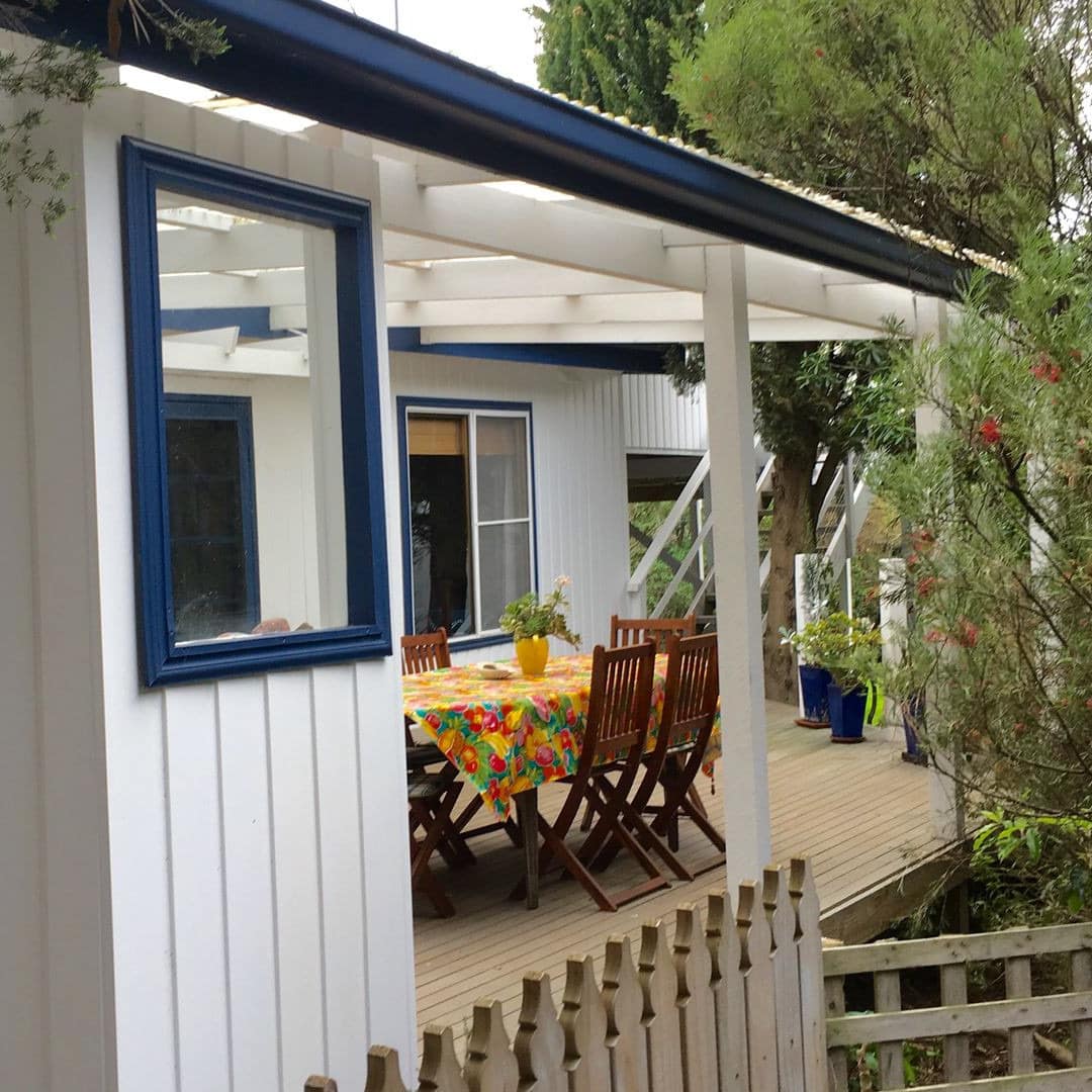 Lively wood deck on blue- and white-painted beach house with a pergola and outdoor dining table