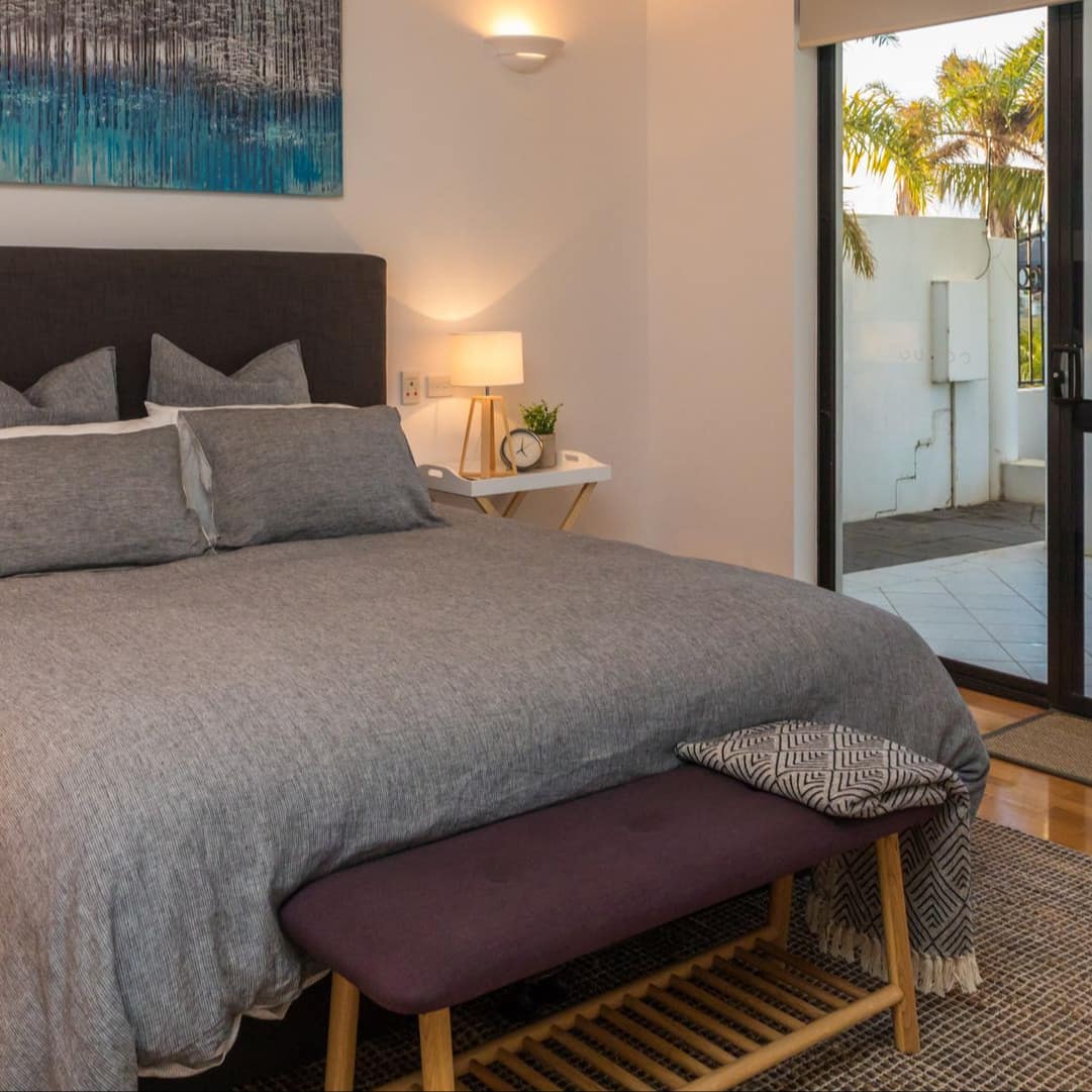 Bedroom with hardwood floors, a king size bed, grey bedding, matching wood bedside tables, and glass door to patio.