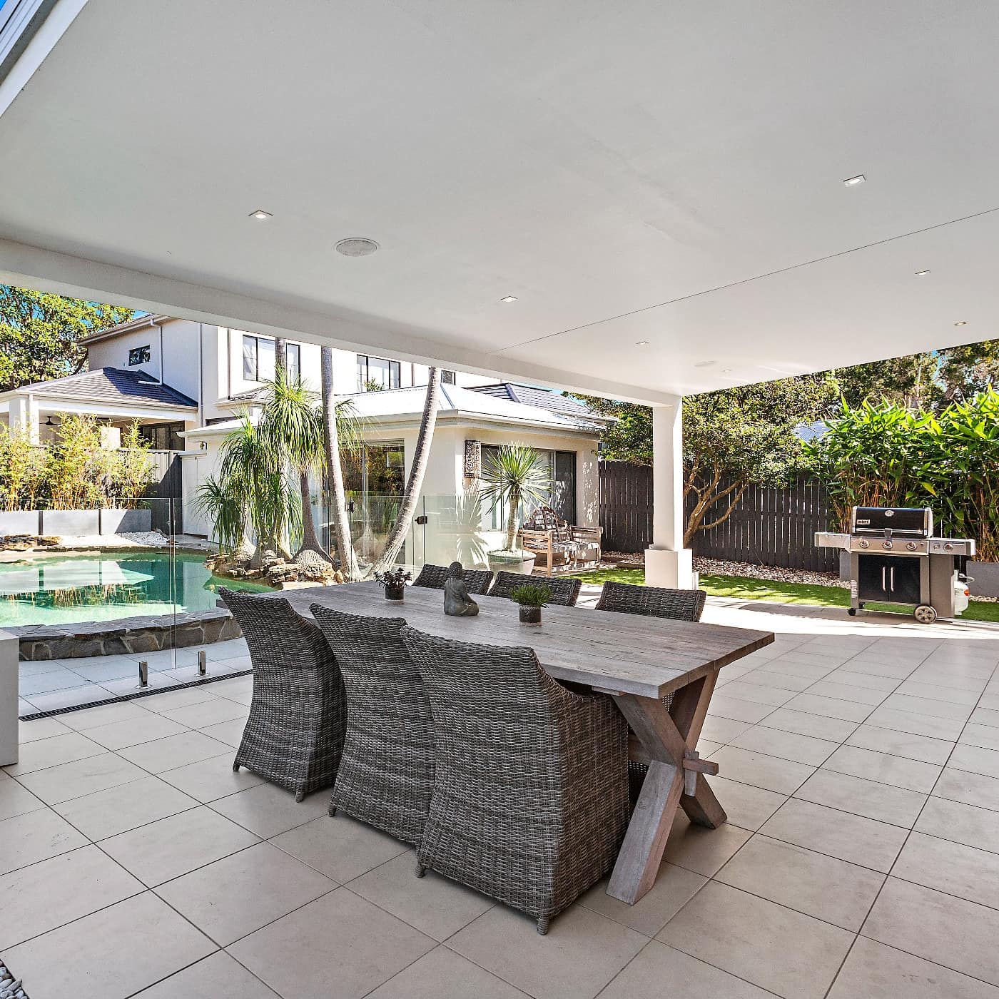 Outdoor patio with dining table and view of home and aqua blue pool in the background