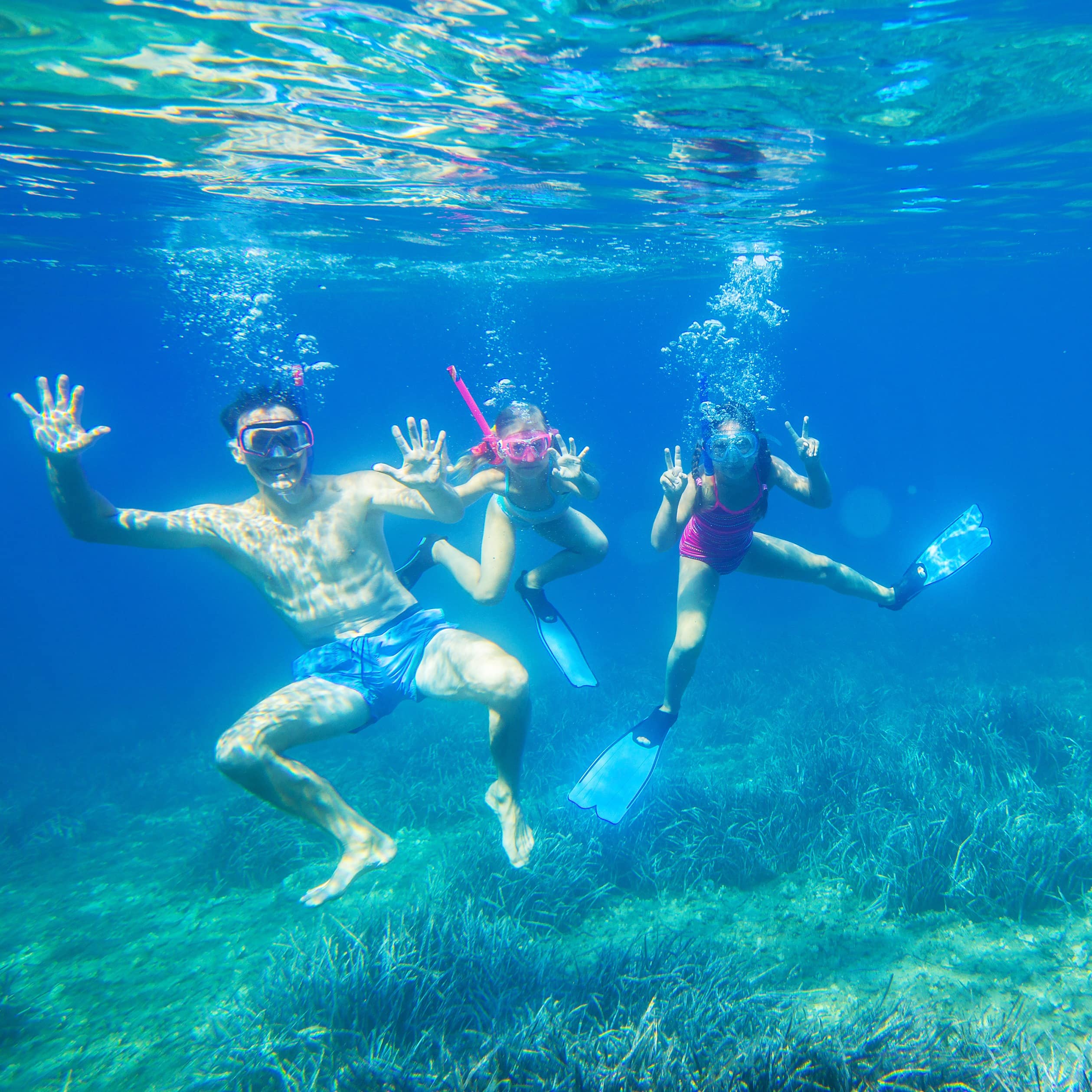 Family of three dive into the sea in masks, making hand signs
