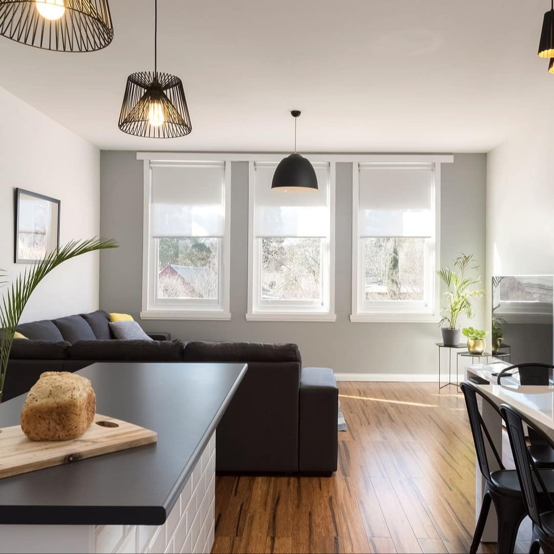 Modern kitchen and living room, hardwood floors, black countertops, white dining set, black sections, and flat-screen TV.