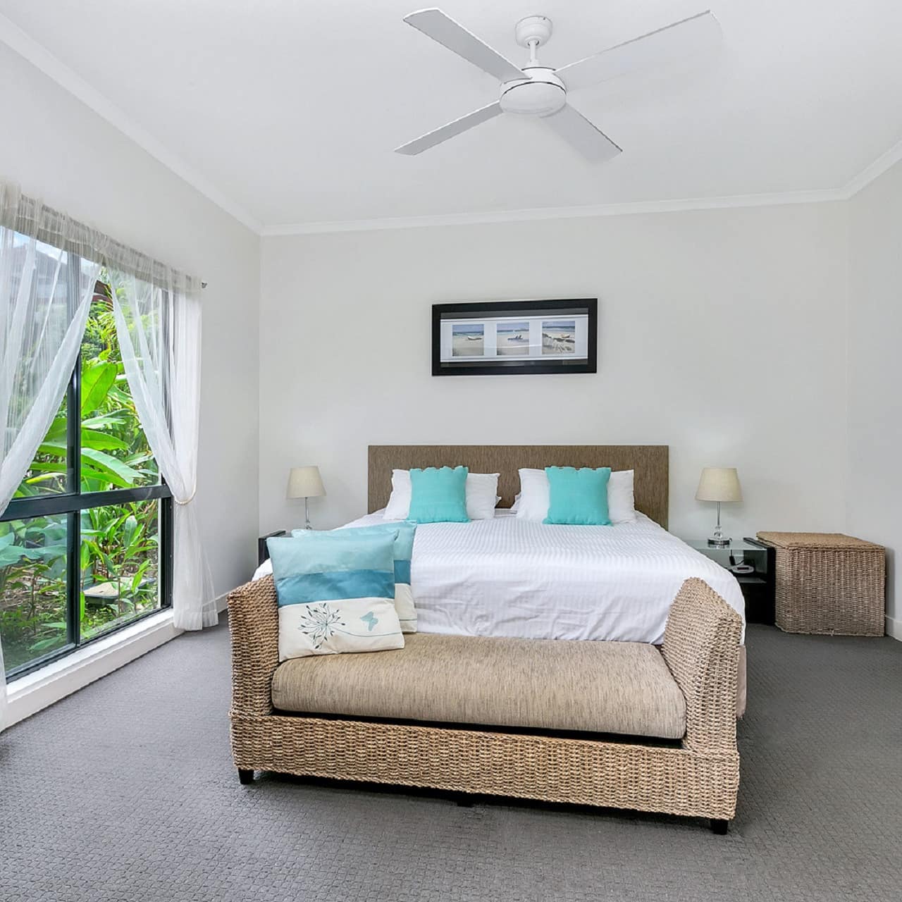 Spacious bedroom, grey carpet, white walls, a king size bed, blue and white bedding, wicker furniture, wide window.