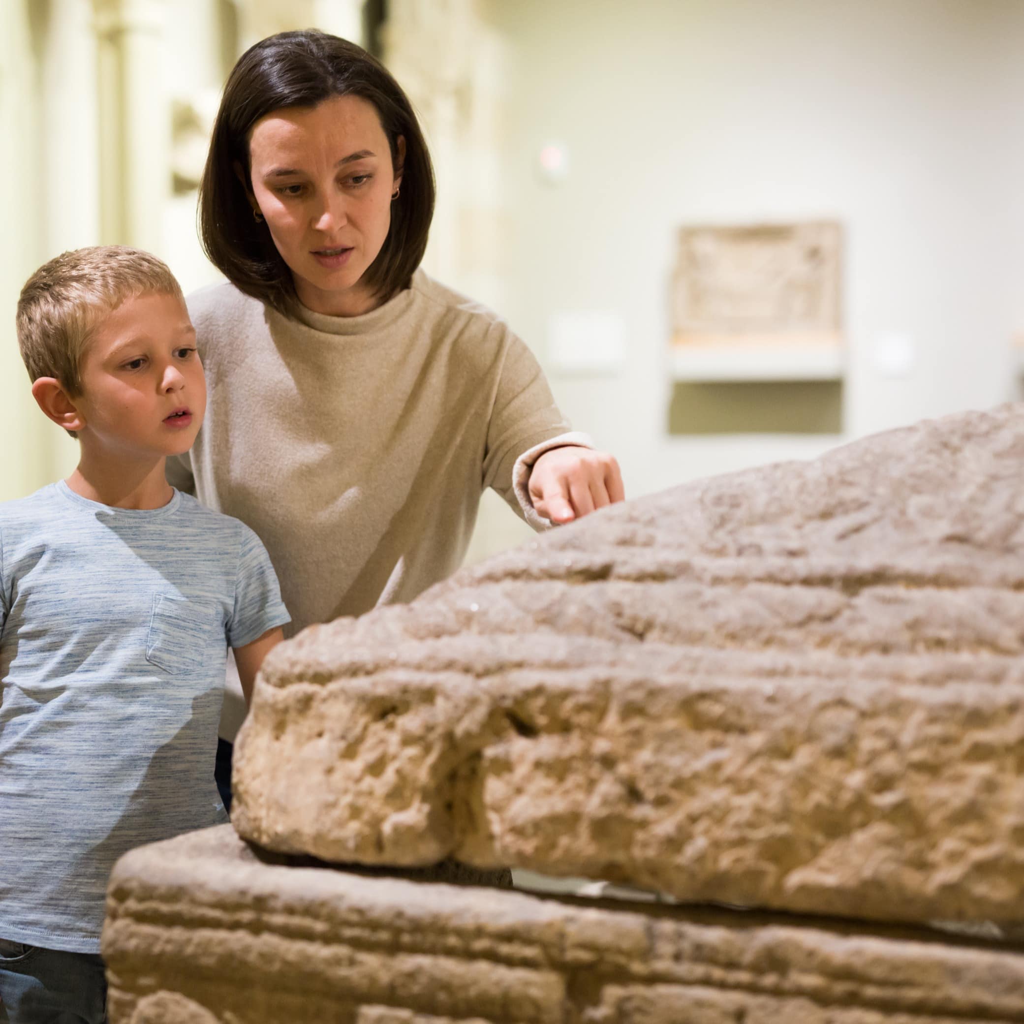 Mother with son observing with interest sculptures exhibition in art museum