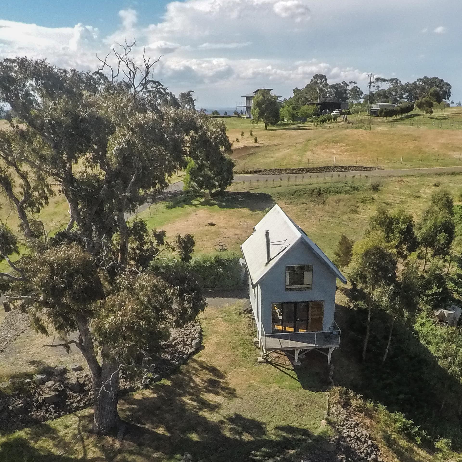 A 2-storey white, elevated spa villa with a front porch and windows sits in the bushland amidst the trees