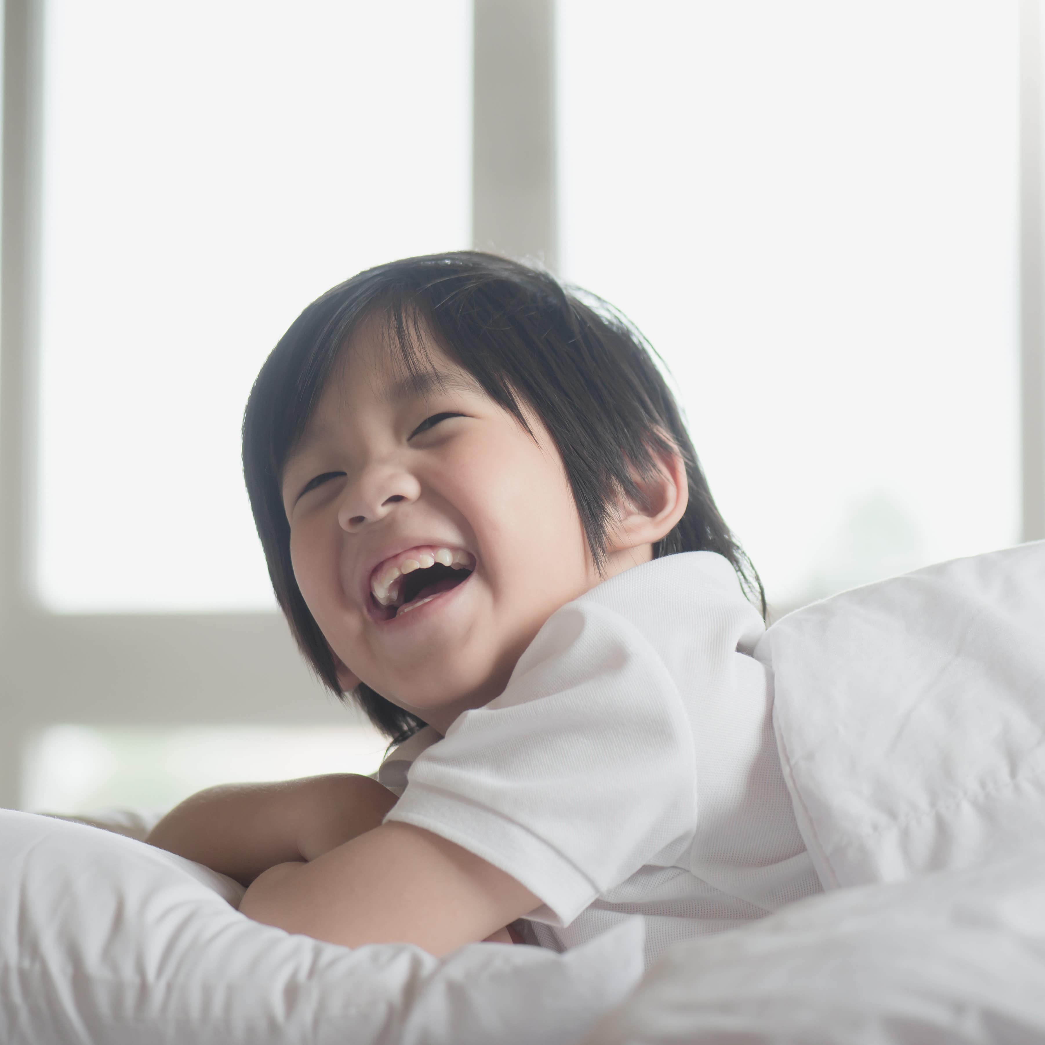 Happy child on a bed in a hotel waking up with blurred background