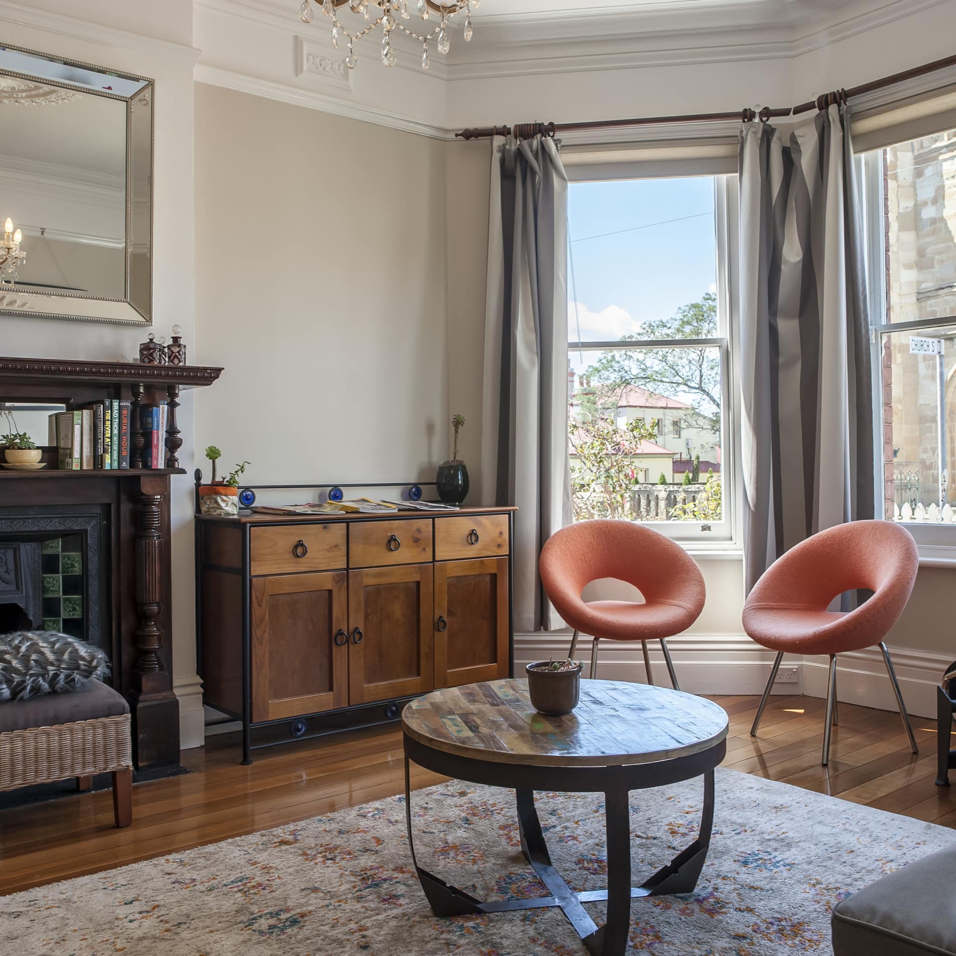 Eclectic living room with hardwood floors, a fireplace, orange round chairs, wooden coffee table, and tall bay windows.