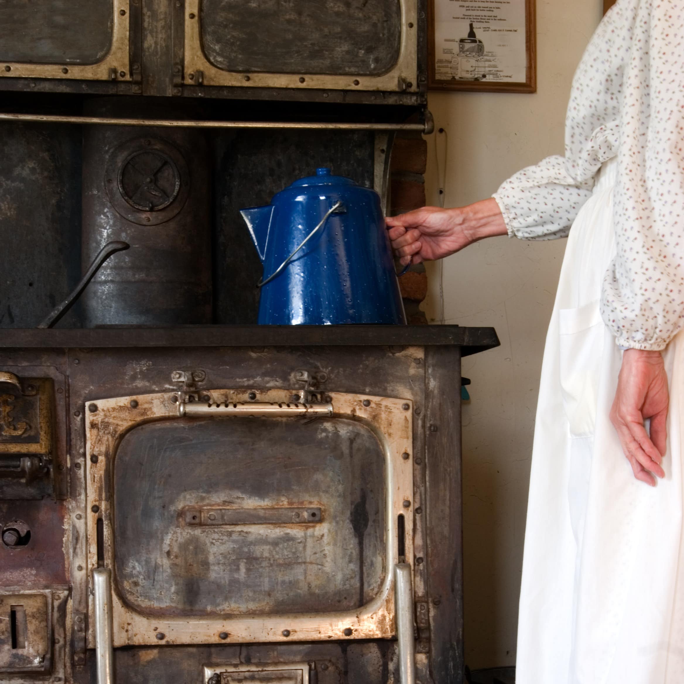 Body of lady touching kettle while standing by an antique wood stove in museum