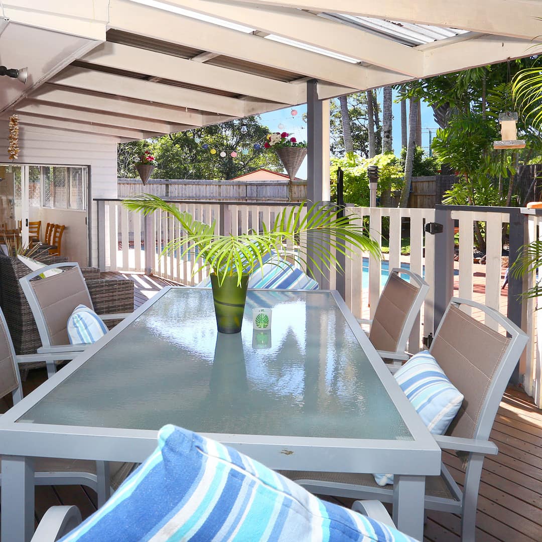 Veranda of beach cabin with outdoor dining table looking out on private pool and gardens