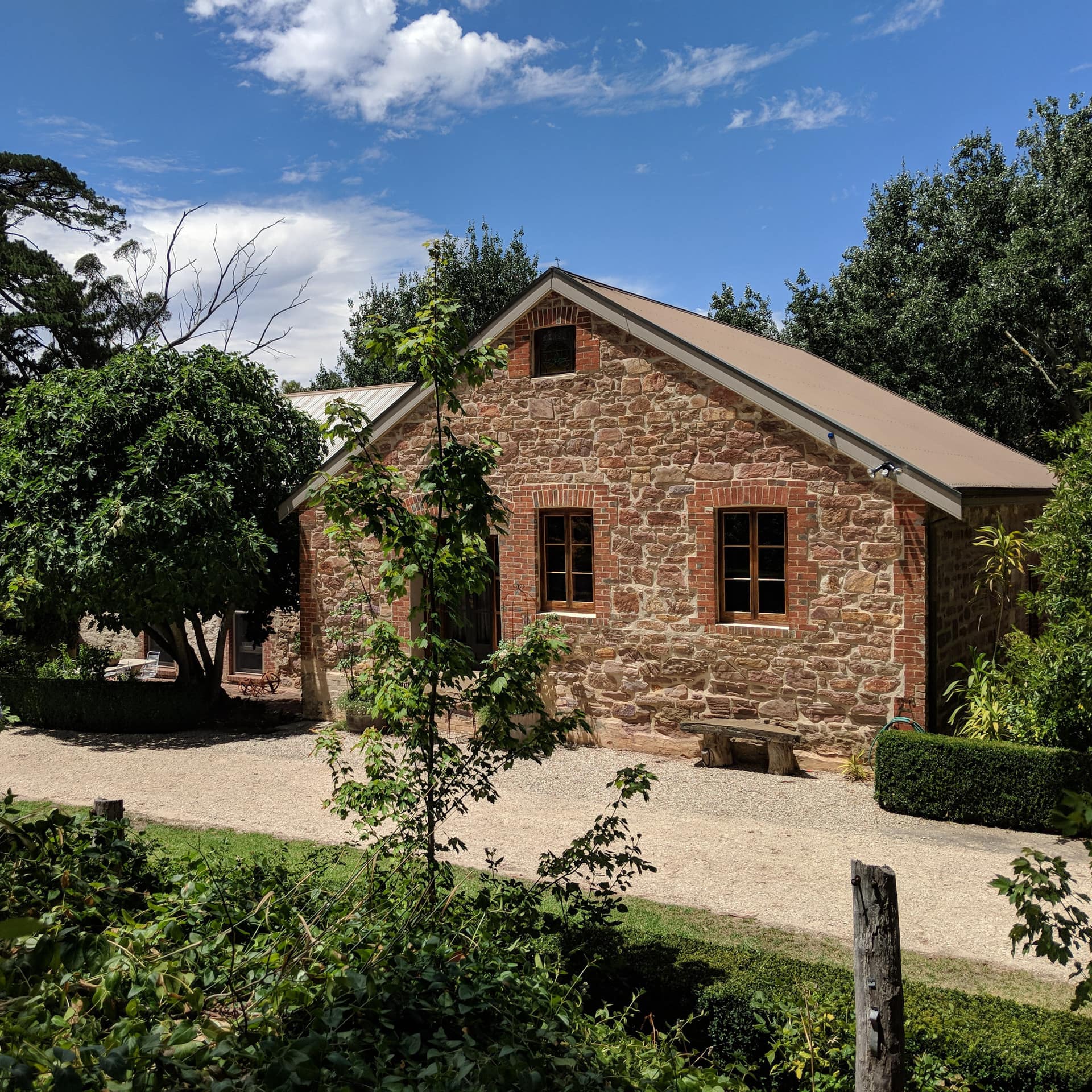 A cottage with natural stone siding, pebble gravel driveway and lush garden.