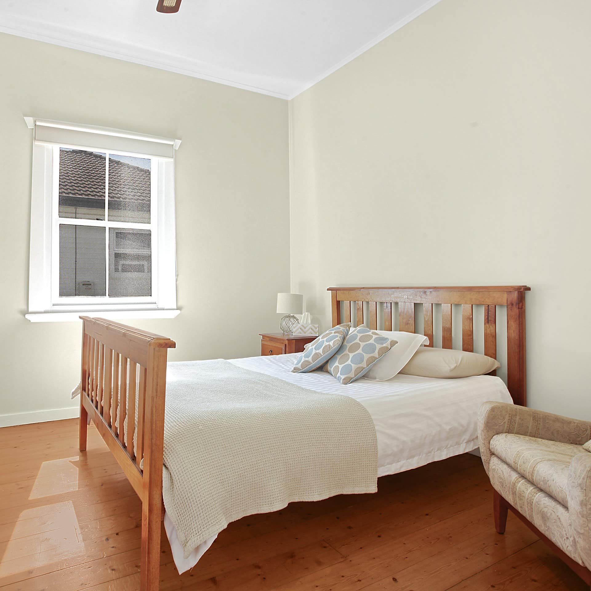 Spacious and bright bedroom with hardwood floors, beige walls, wood framed king size bed, beige and white bedding.
