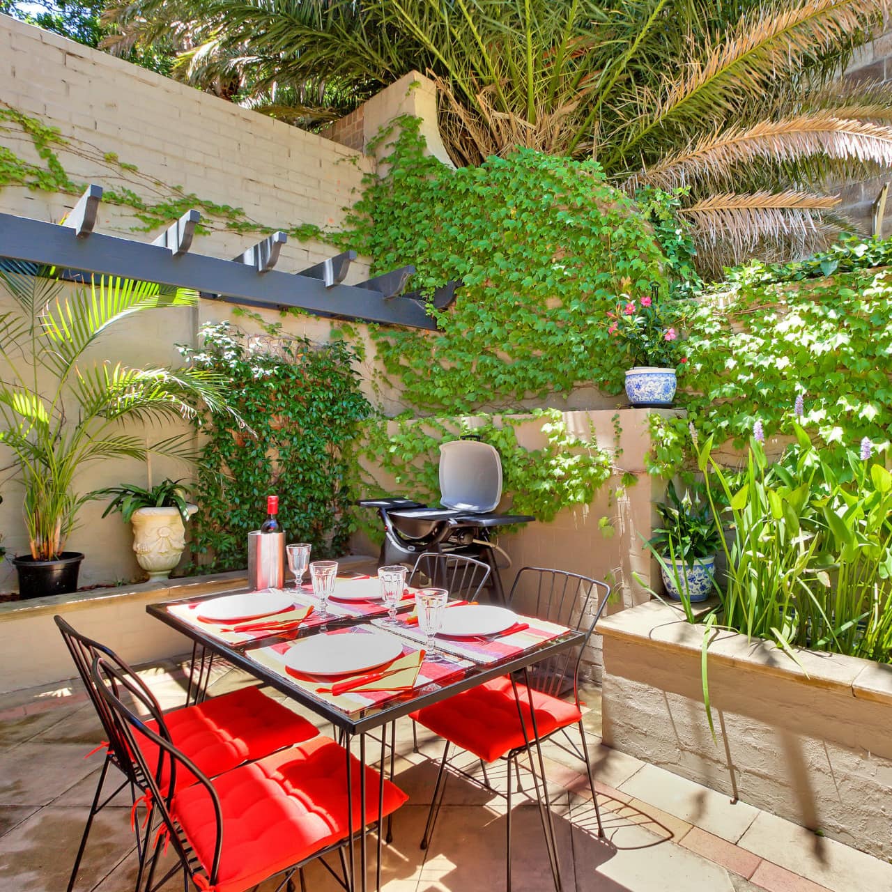 An enclosed, sunny patio with ivy and vegetation surrounding the space, and black wrought iron table and chairs.