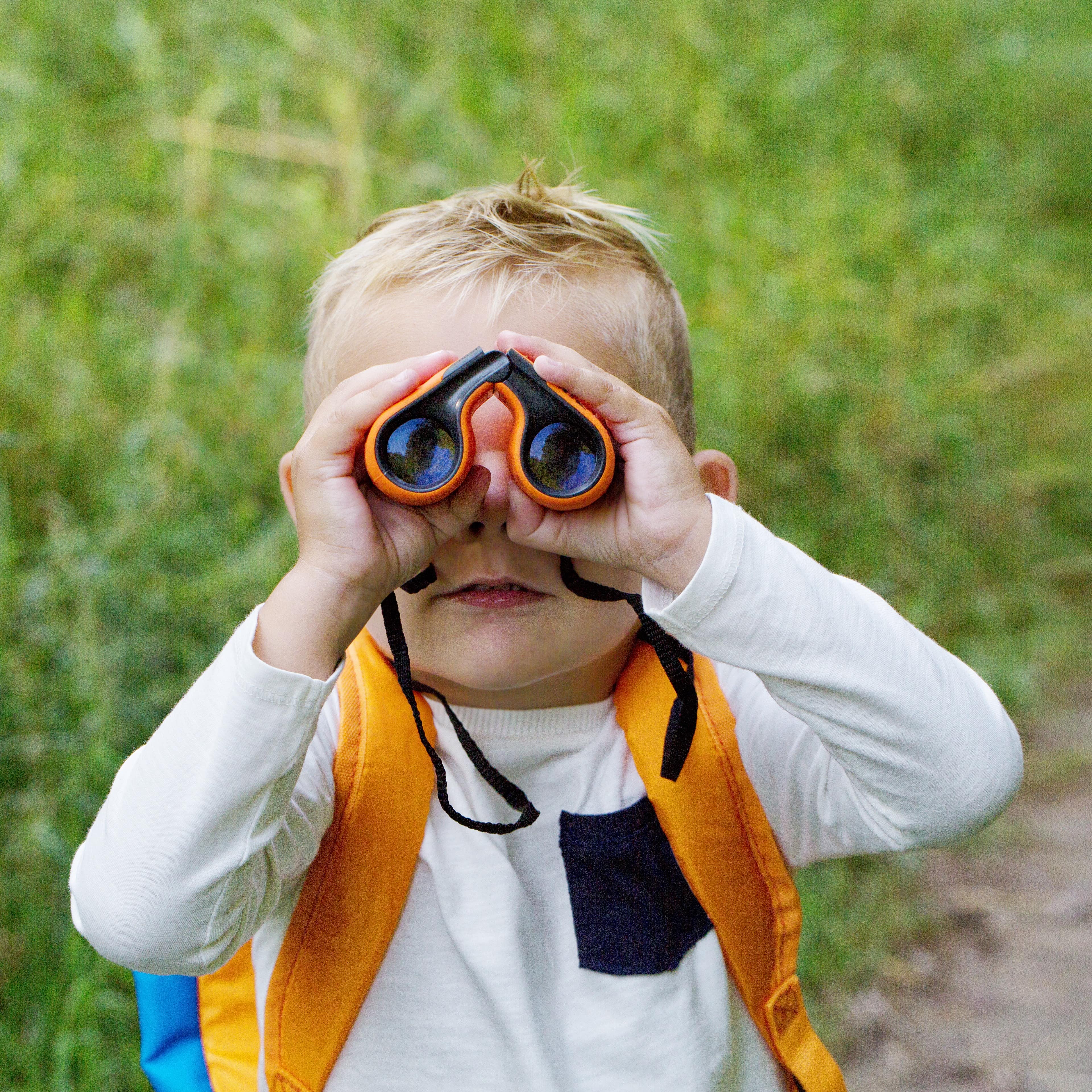 A little boy young researcher exploring with binoculars and backpack
