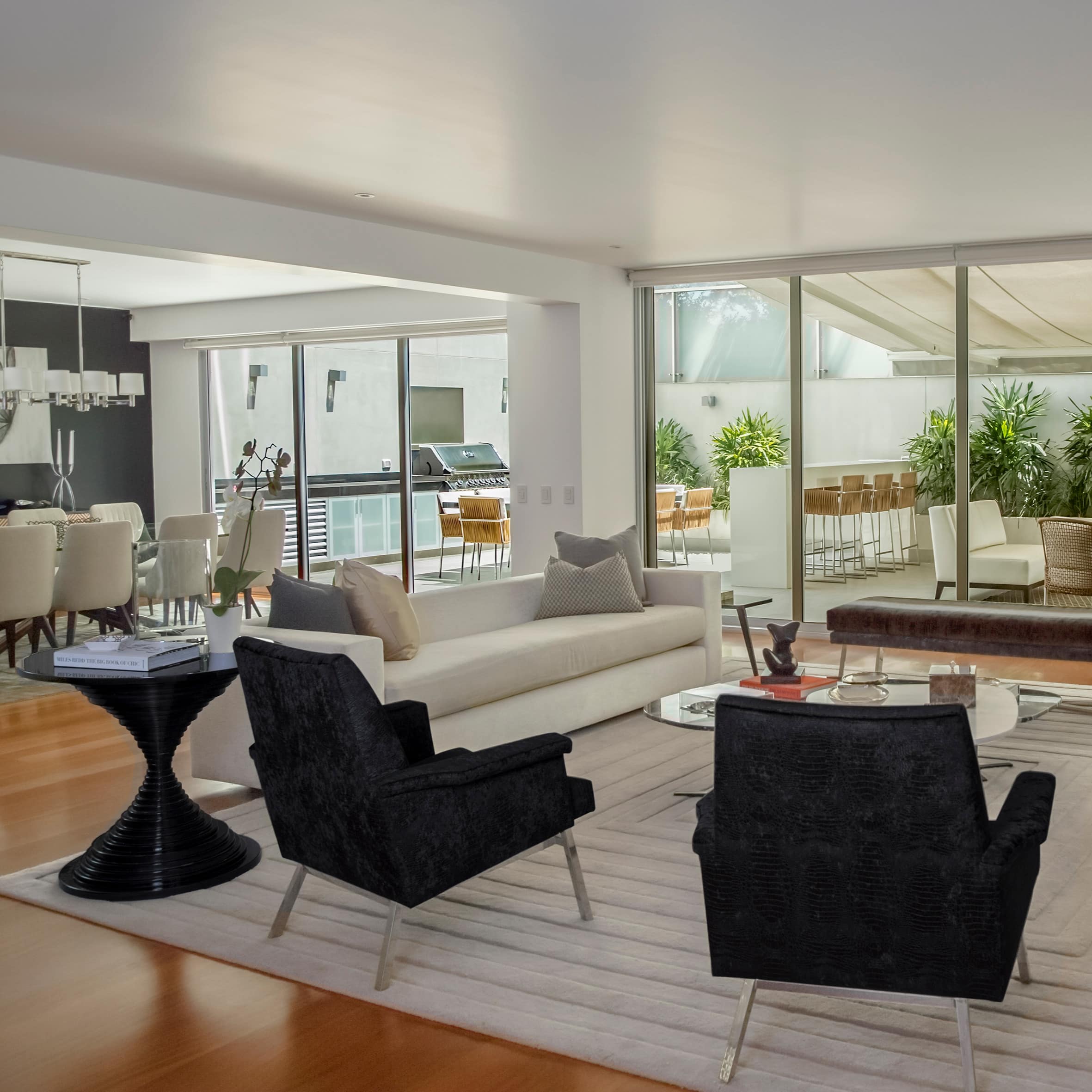 Open living and dining area with wood floors, contemporary black furnishings in white surrounds with patio and sunroom