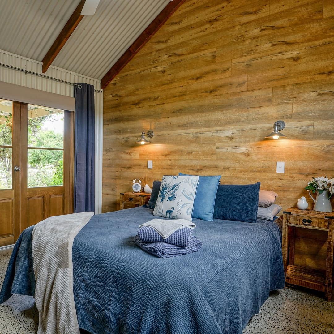 Rustic bedroom with wood-panelled accent wall, a king-size bed with blue bedding, double glass door to patio space.