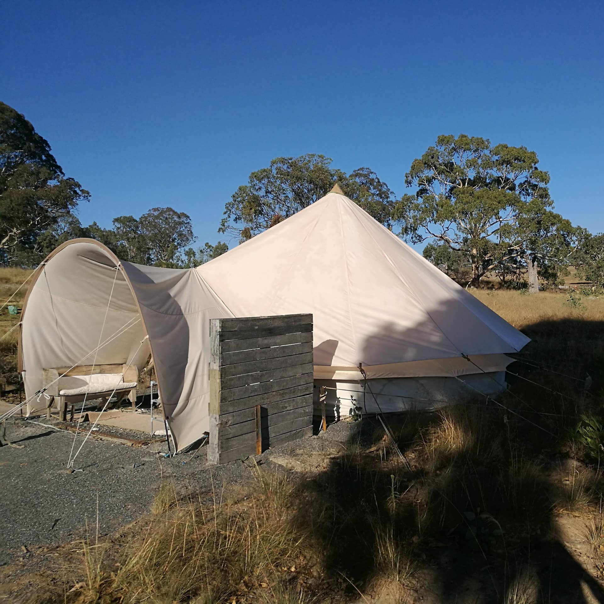 White, tipi-style tent with open entrance surrounded by lush, rural landscape.