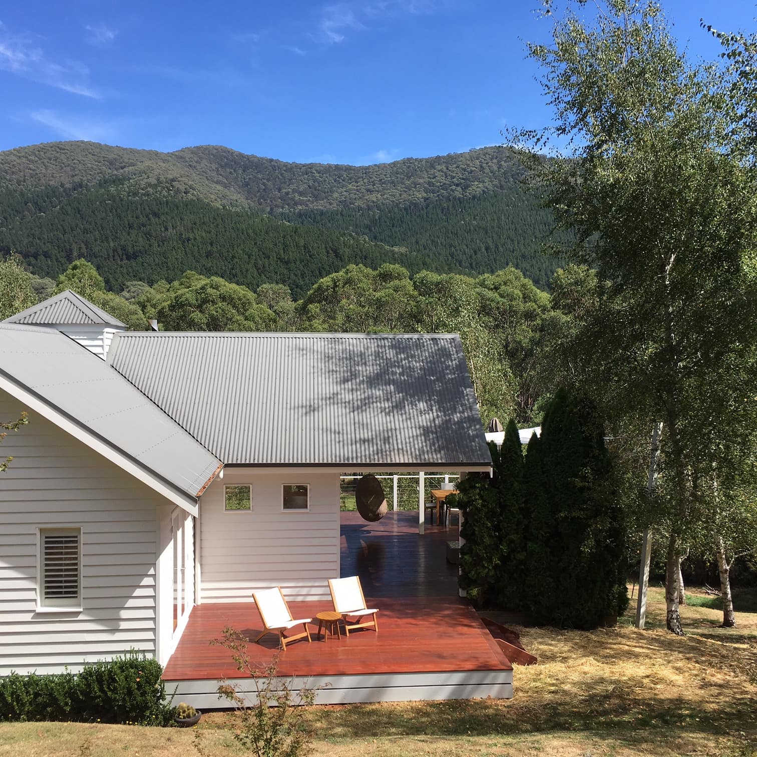 Charming home with white siding, grey roof, and partially covered wooden deck overlooking mountainous landscape.