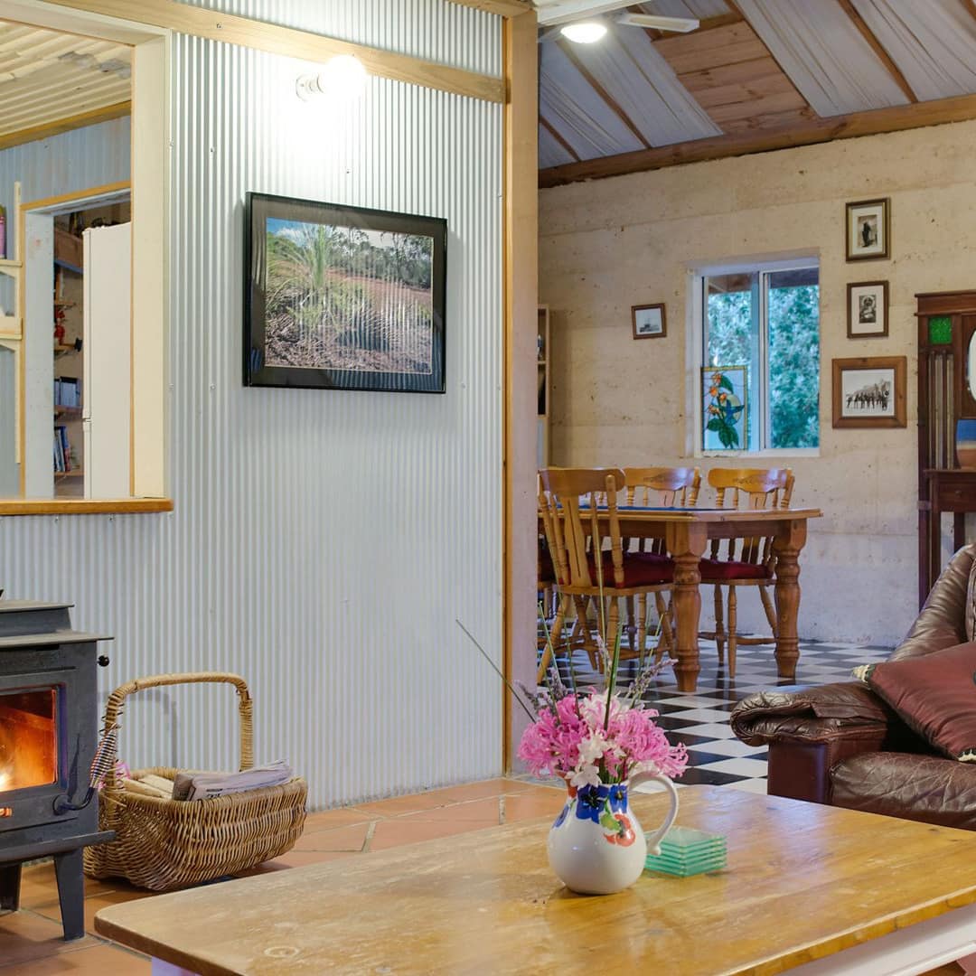 Rustic living room with a brown leather sofa, wooden coffee table, wood-burning stove, and wooden dining set.