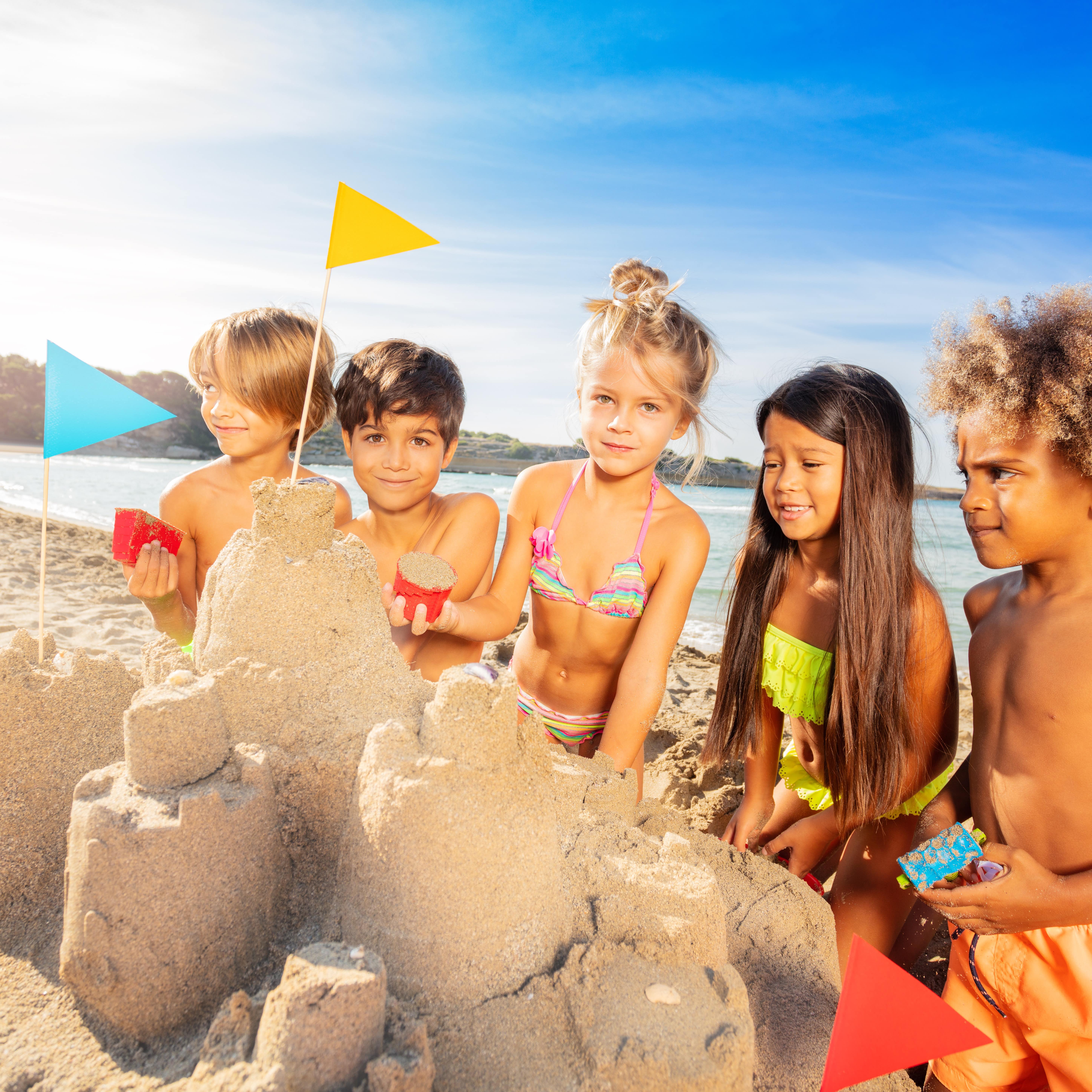 Five happy kids creating sandcastle using sandpit toys at the beach