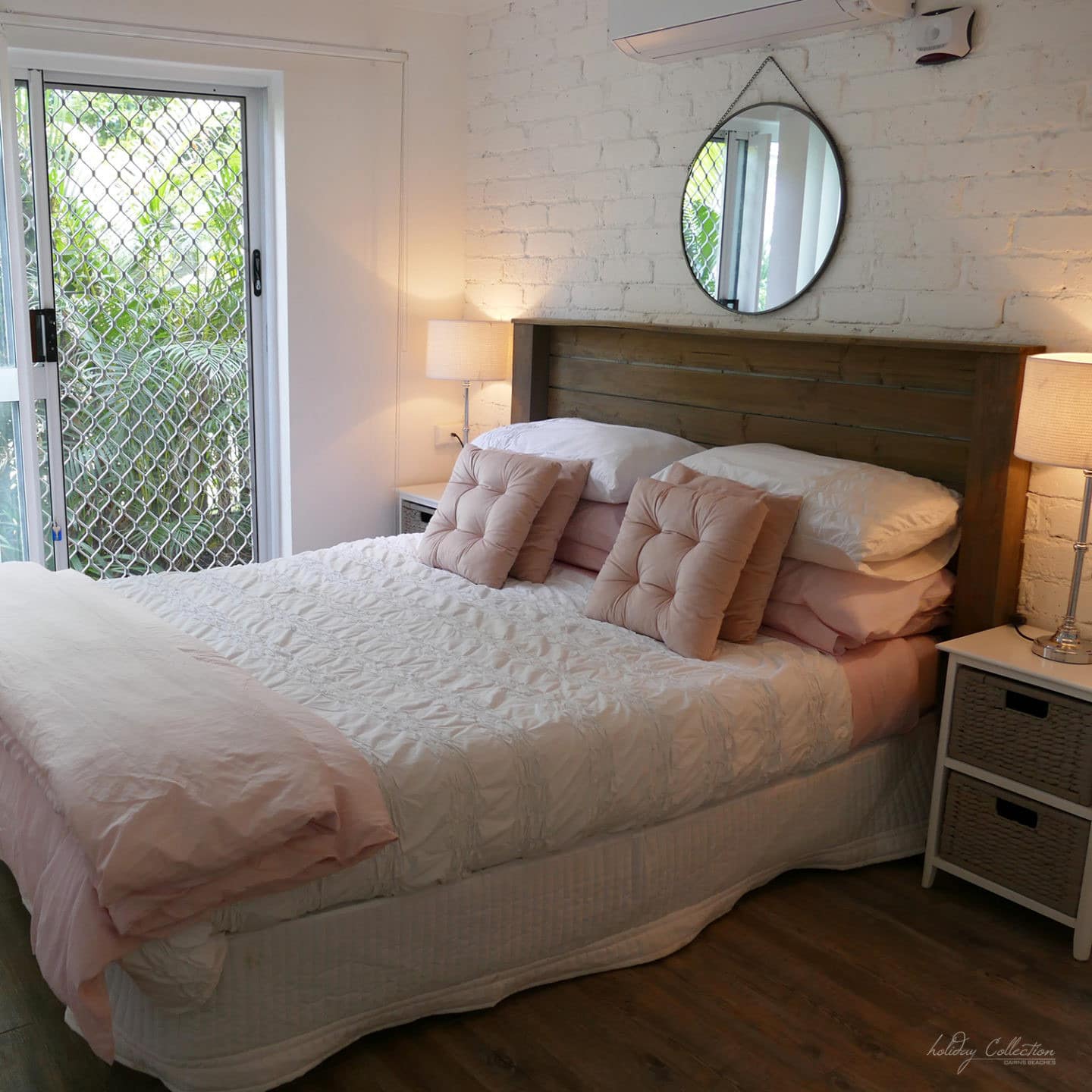 Lovely bedroom with queen bed, soft-pink linens and hardwood floors set against painted brick wall with sliding glass door