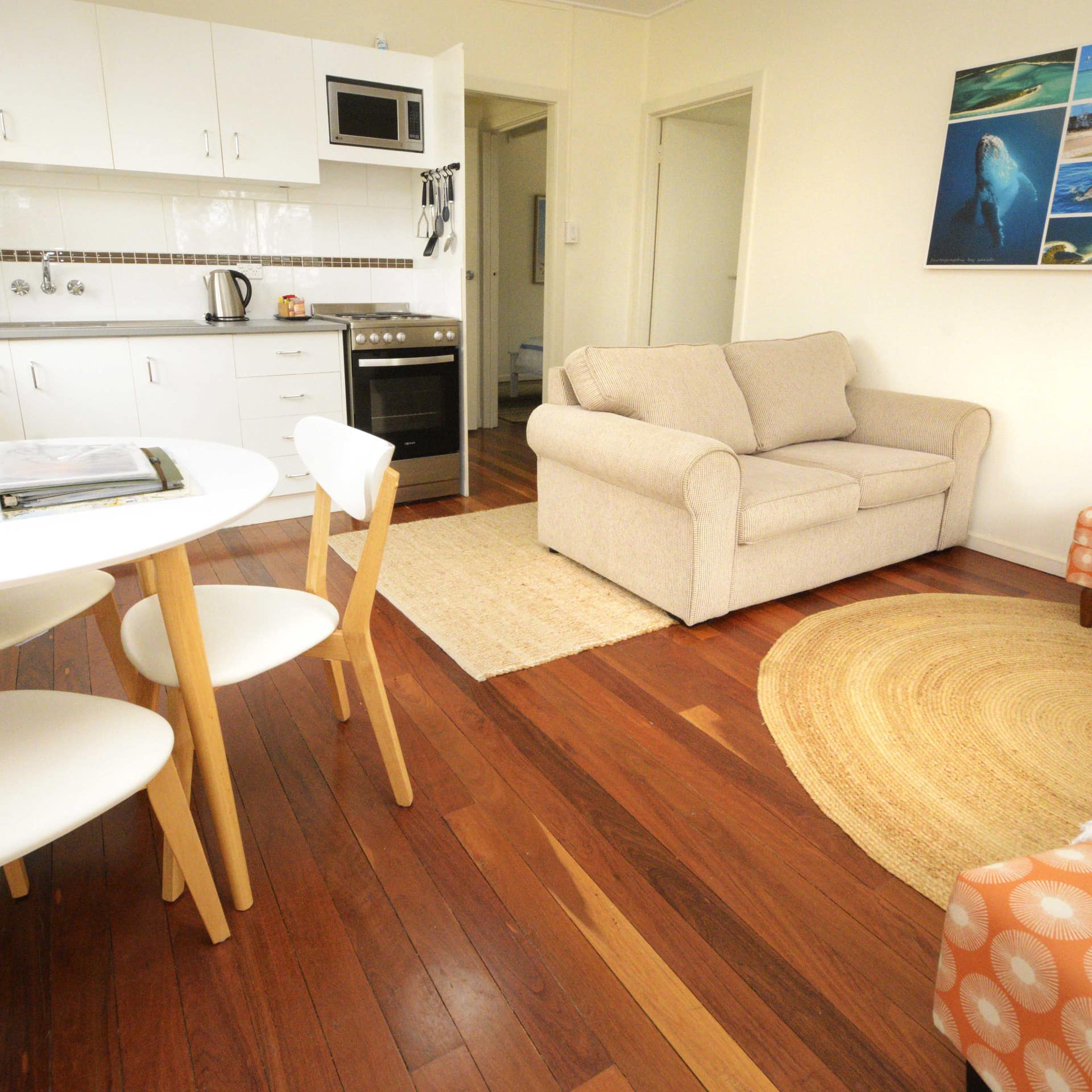 Open living, dining and kitchen area with a modern white table and chairs, light brown sofa, woven rug, and wood floors.