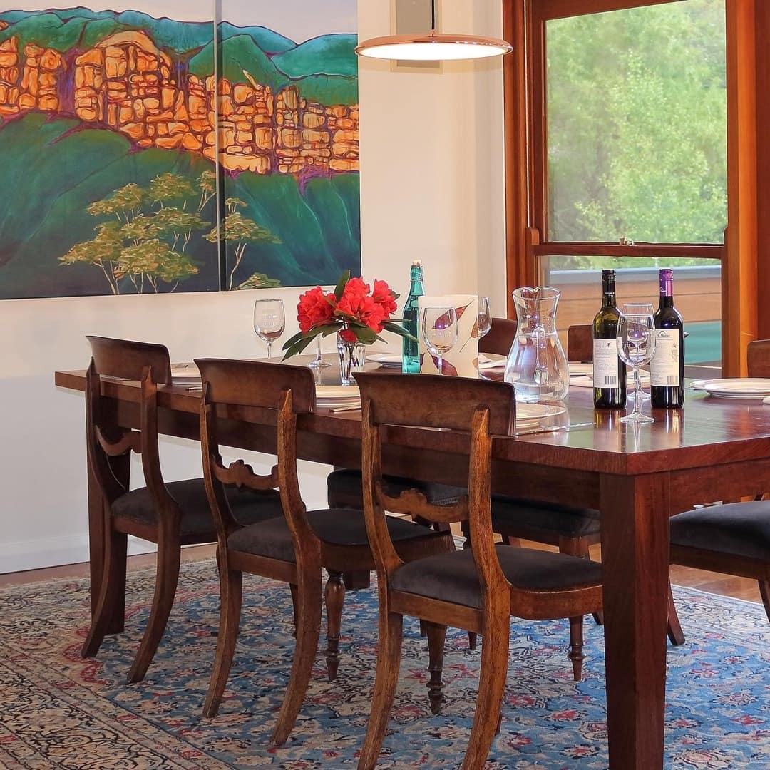 Dining room with large windows that look out on a balcony with mountain views, cherry wood dining room set, and persian rug.