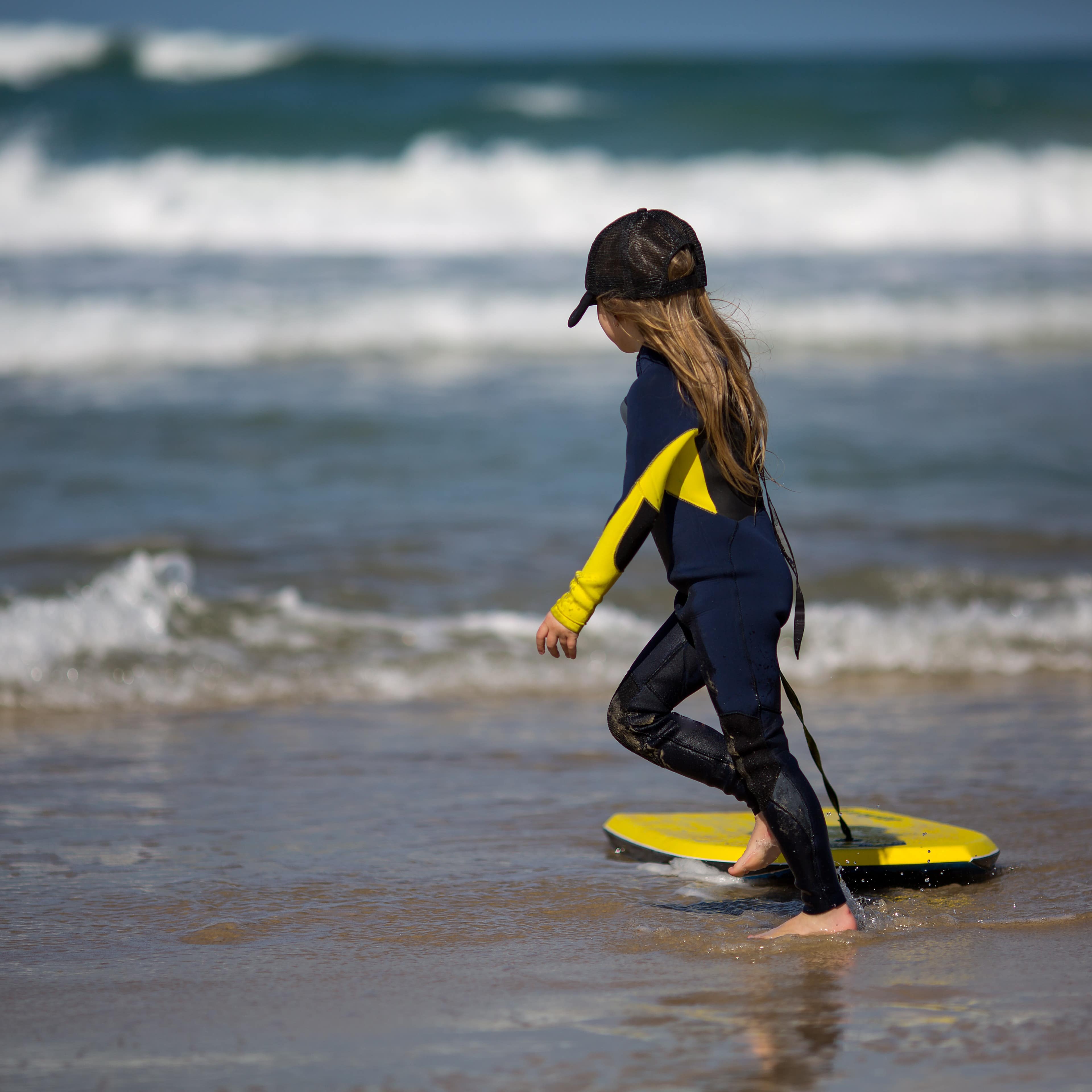 Little girl pulling her surfboard at the beach