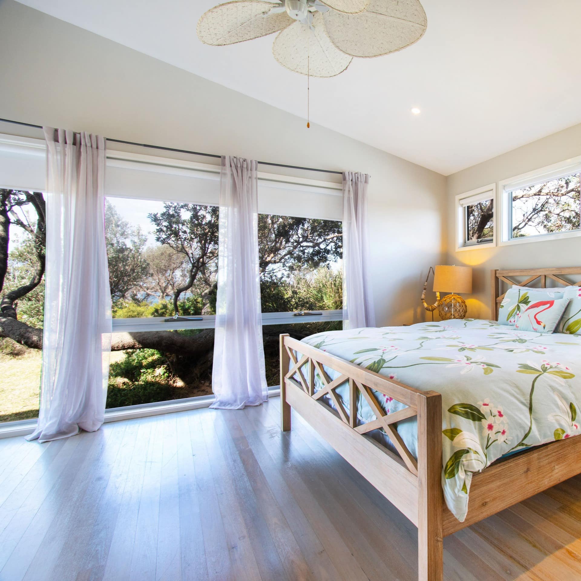 Spacious bedroom with hardwood floors, a king size bed, floral bedding, and tall windows with nature views.