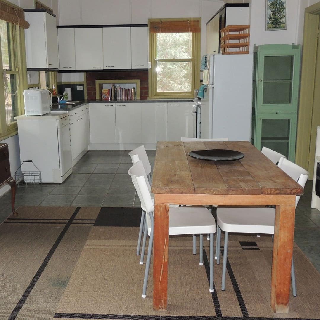 Open kitchen and dining room with grey tile floors, wooden dining set, white cabinets, tan and black area rug.