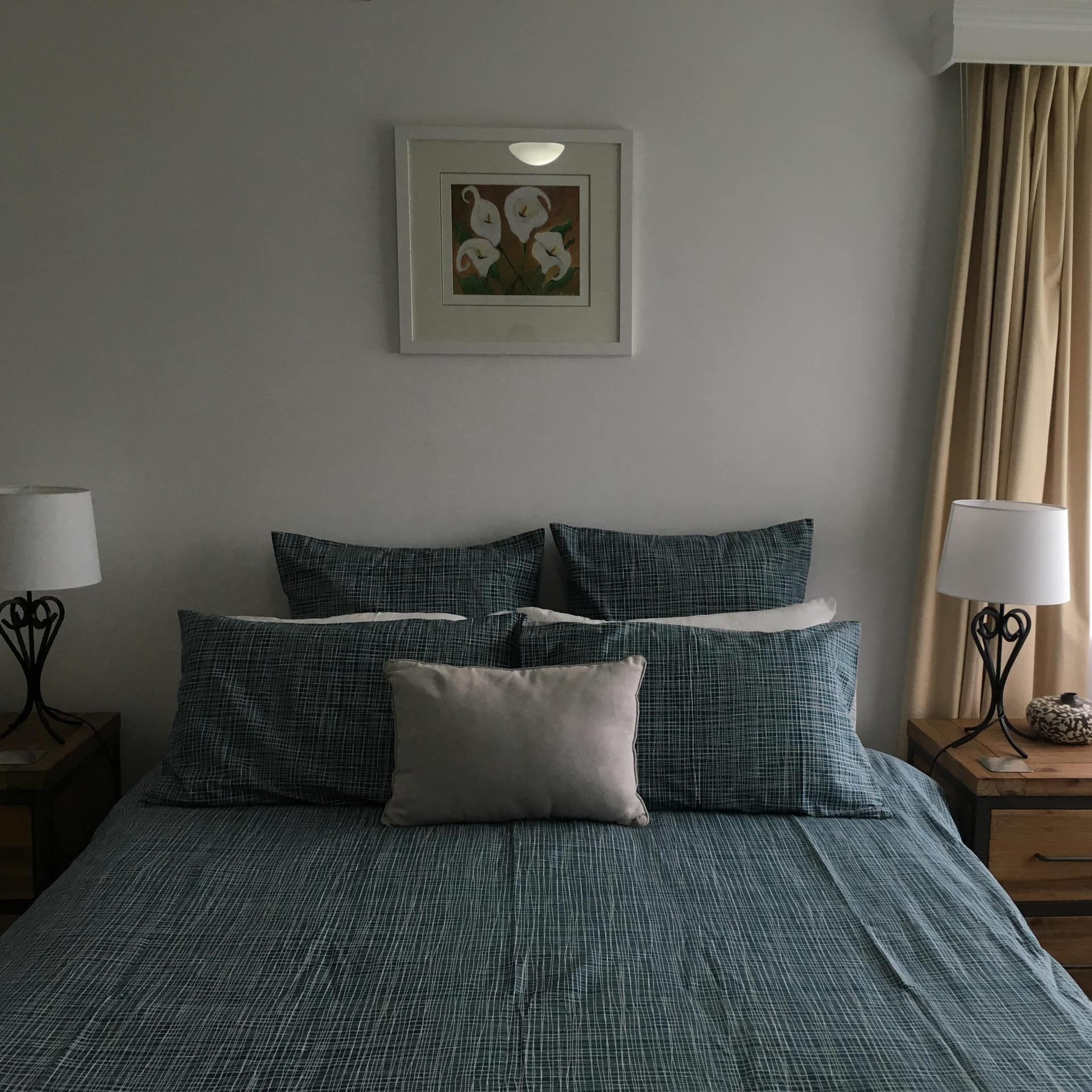 Bedroom with grey walls, queen size bed, blue and grey bedding, wooden bedside tables.