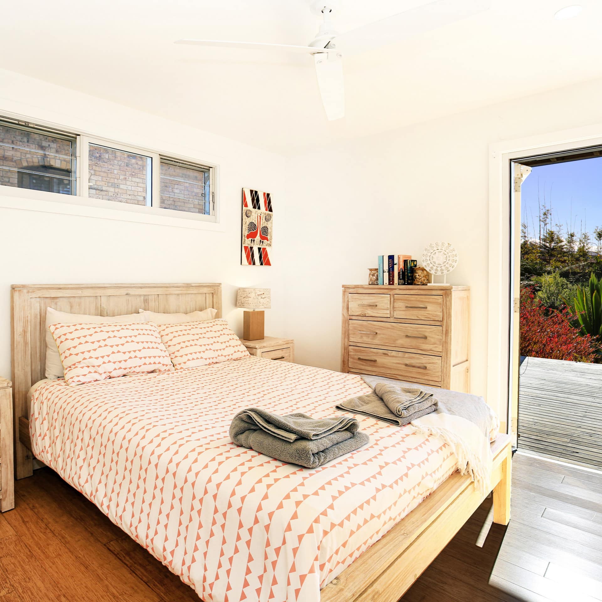 Bedroom with hardwood floors, white walls, a king size bed, red and white bedding, and an open door to patio.