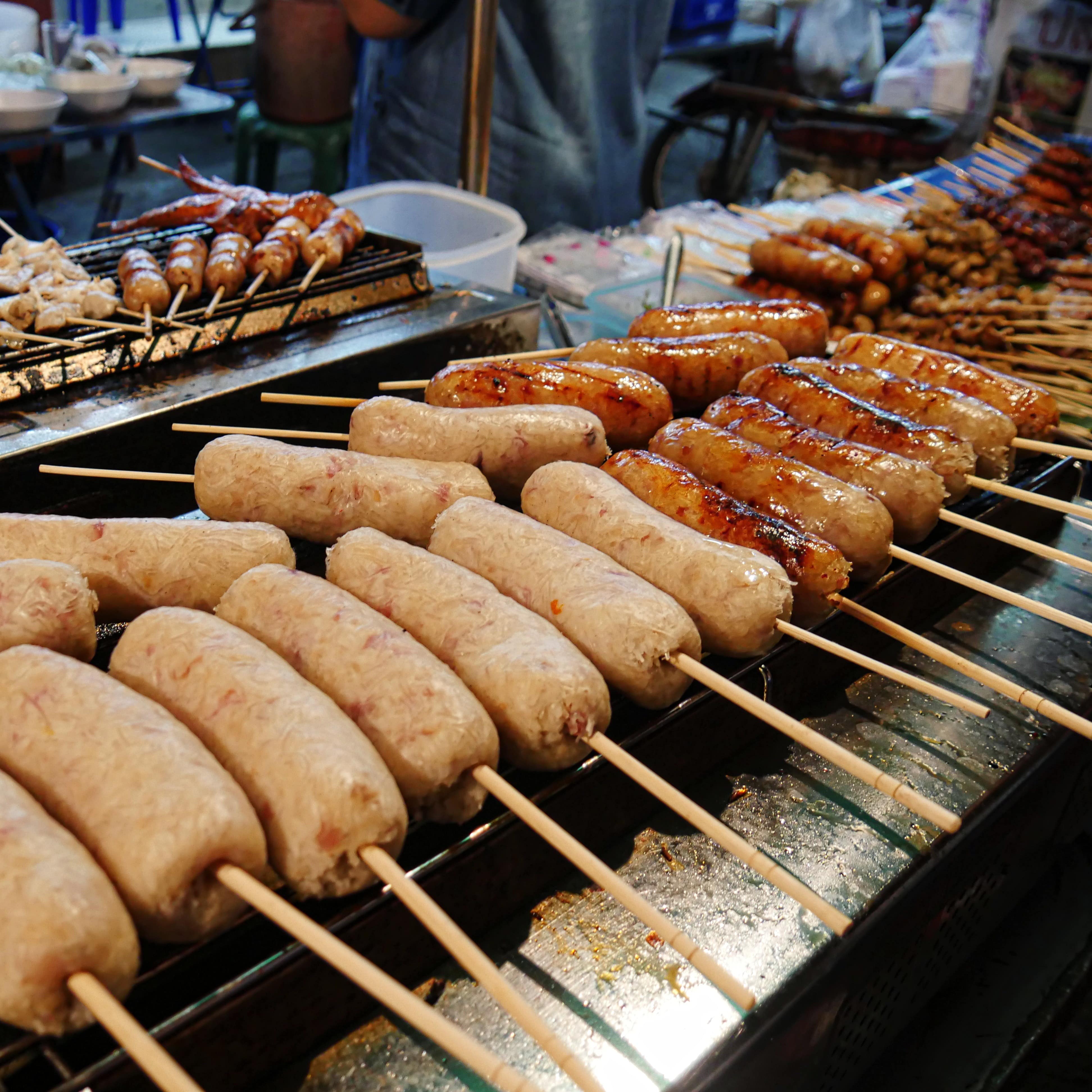 Sausages and other meats on skewers grilling in an open stove at a street market
