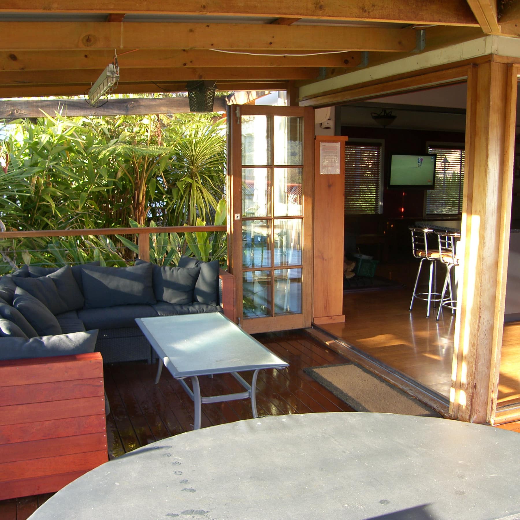A covered deck with a grey sectional, metal table, and folding glass doors to the home’s kitchen.