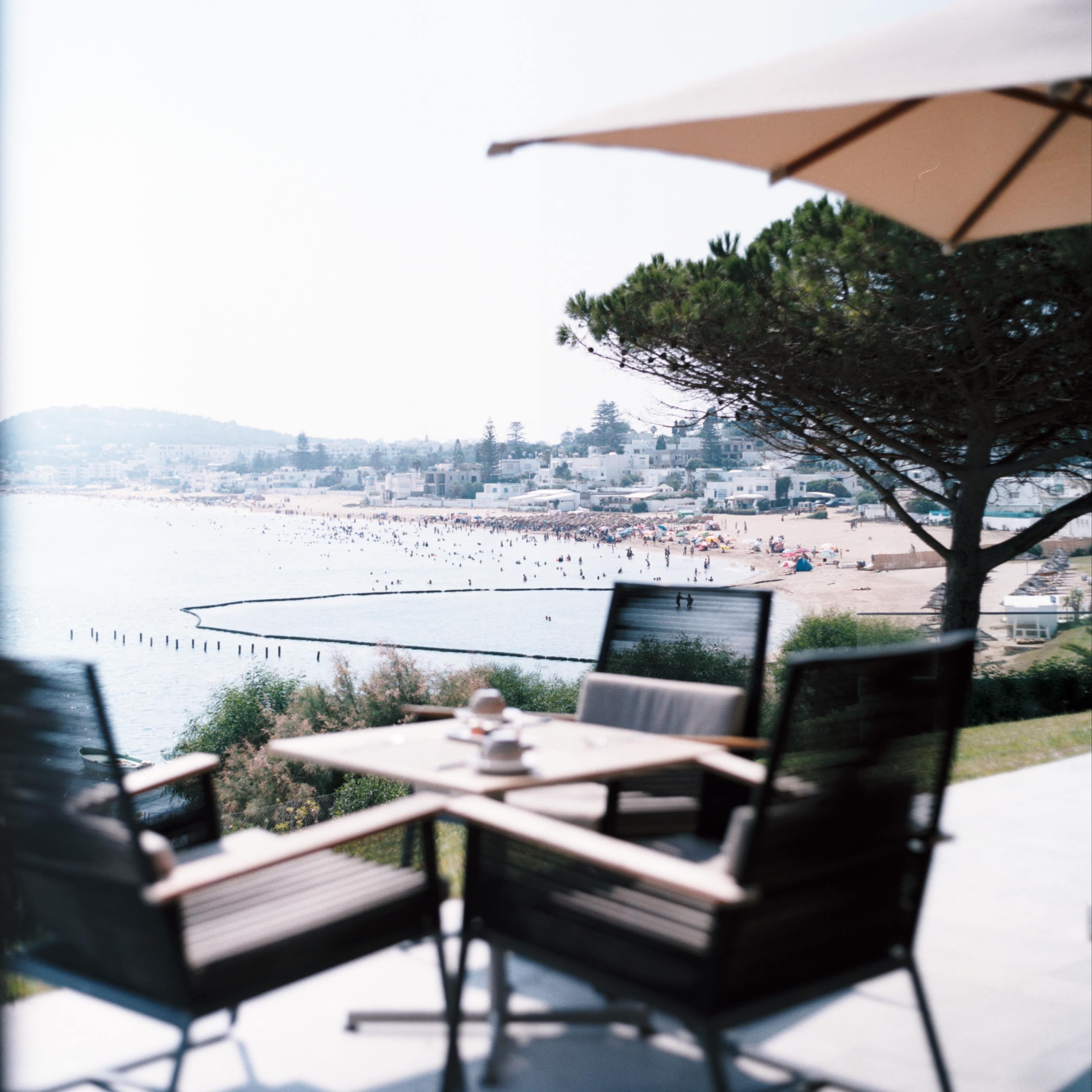 View of the beach from the patio of a hillside villa with a small table and four chairs and houses in the distance